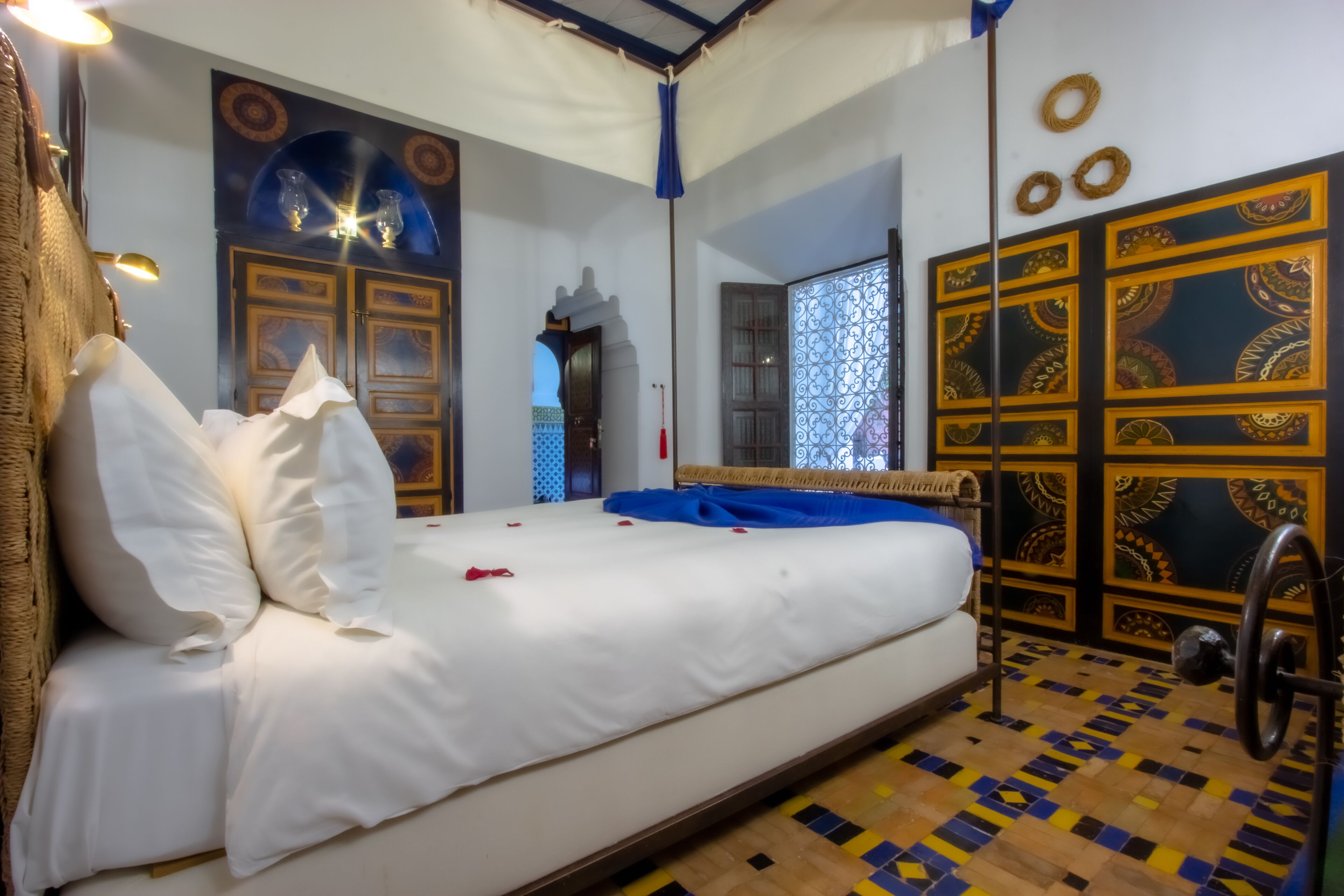 Ein Zimmer mit einem Bett, einem Spiegel, einer Tür mit dekorativen Paneelen und einem gemusterten Boden.