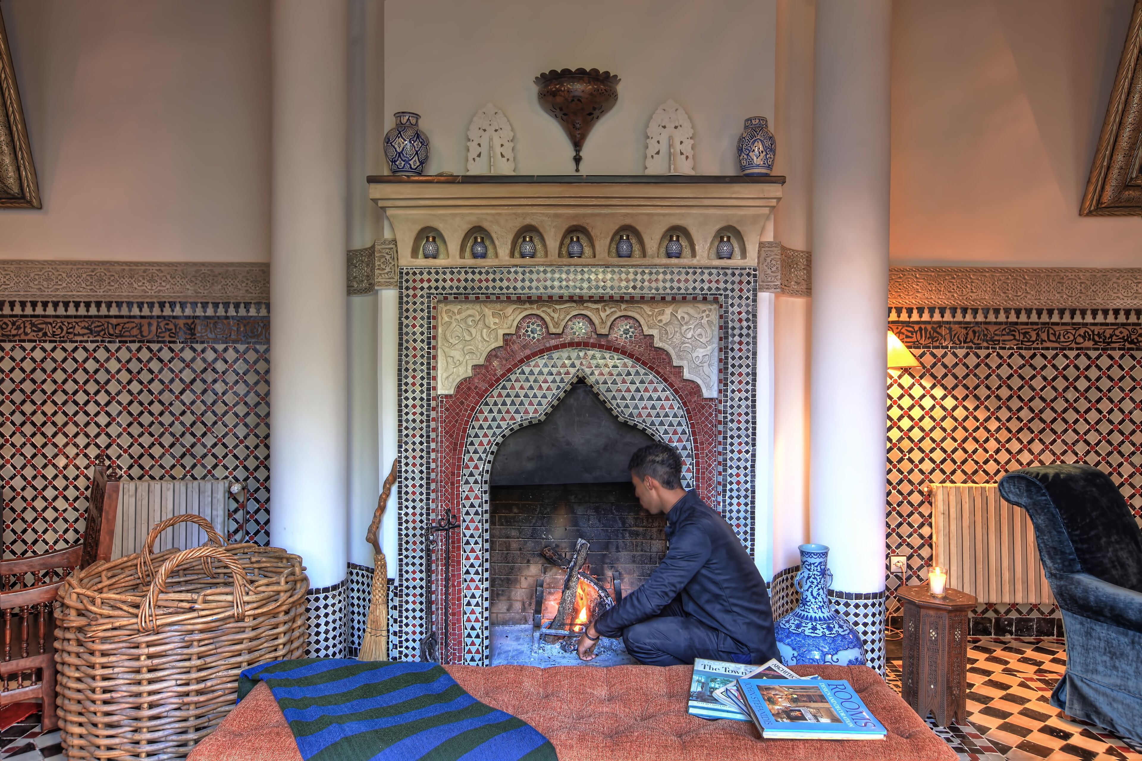 Ein Zimmer mit traditionellem Kamin, gemusterten Fliesen und einer gemütlichen Sitzecke mit Teppich und Kissen.