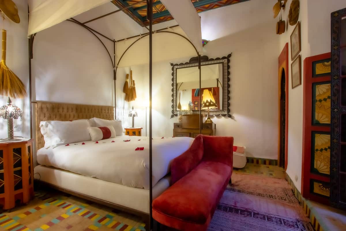A room with a bed, a bench, a mirror, and a patterned rug.