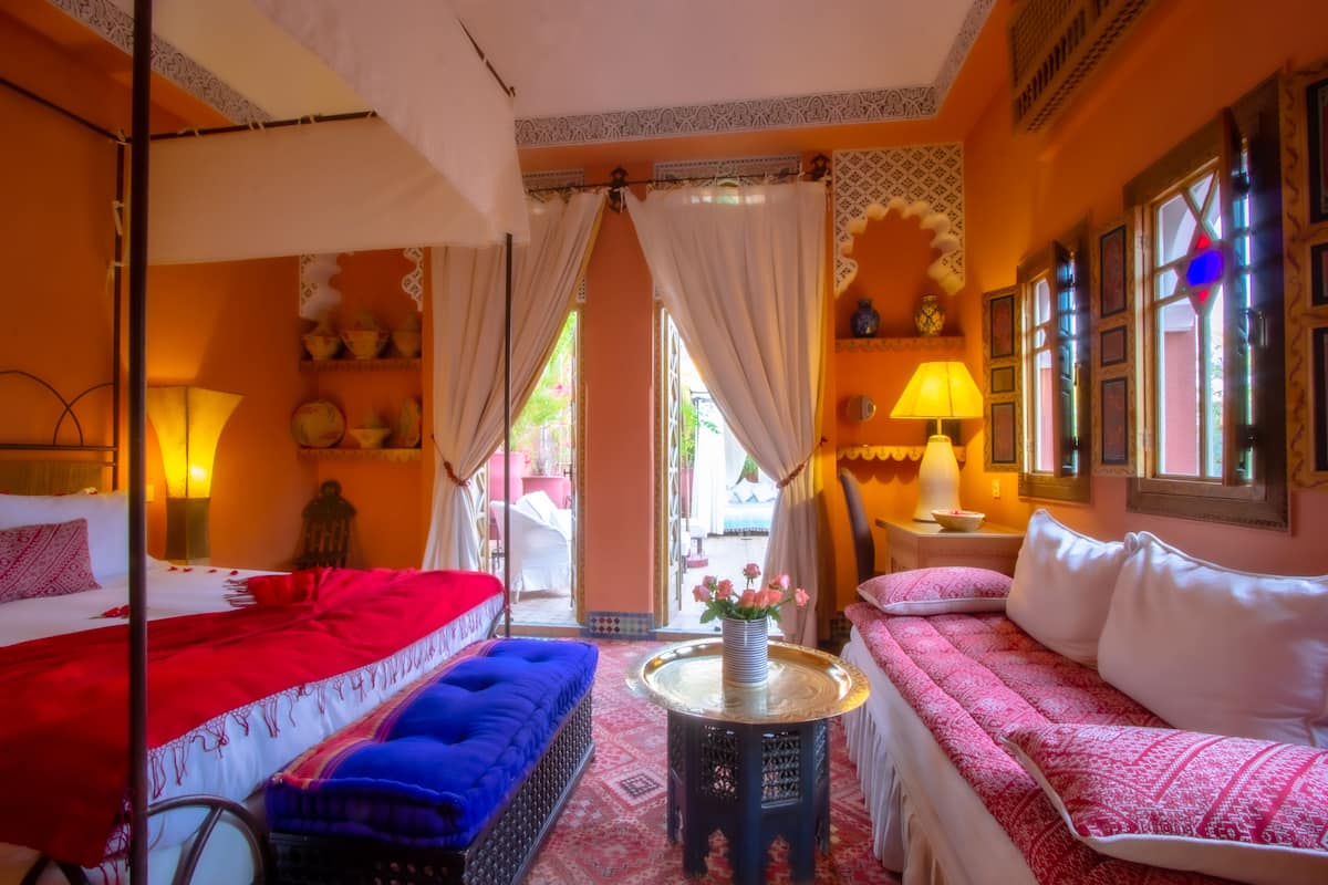 A room with a bed, a sofa, a small table, and a window with curtains.