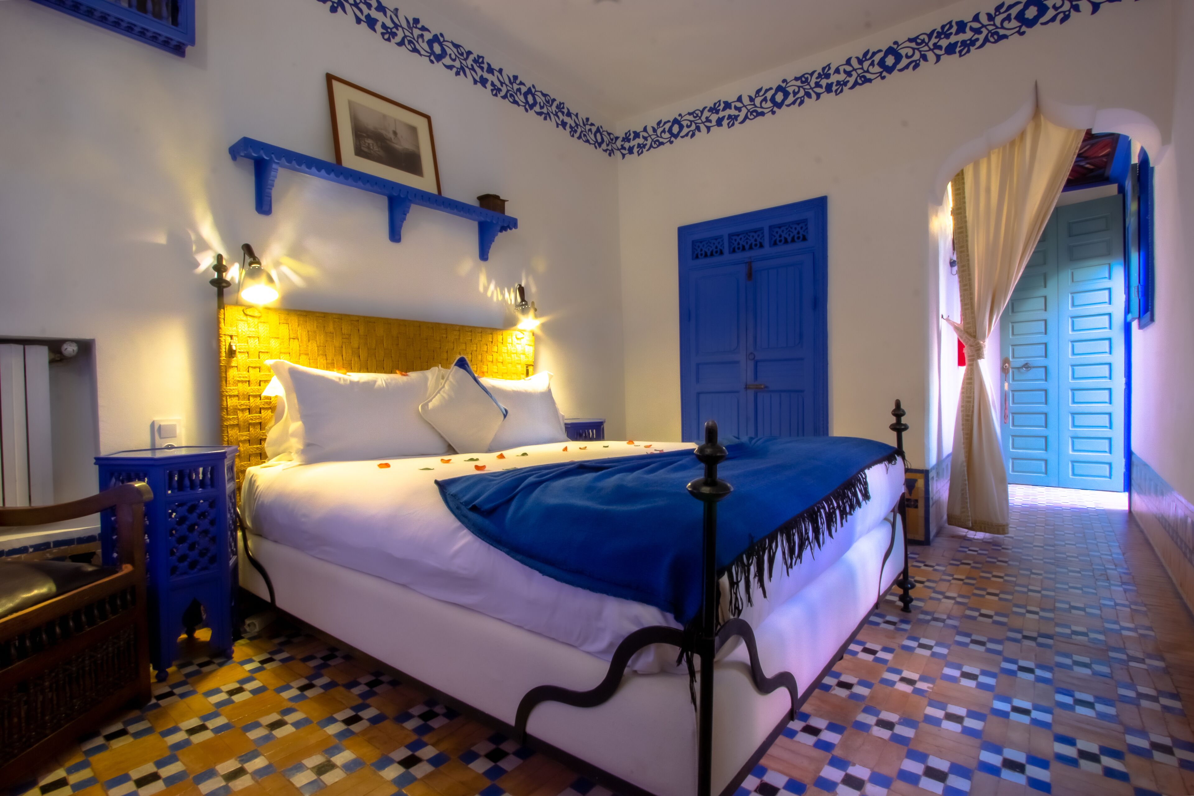 A neatly made bed with a blue blanket, a wooden headboard, and a patterned floor.