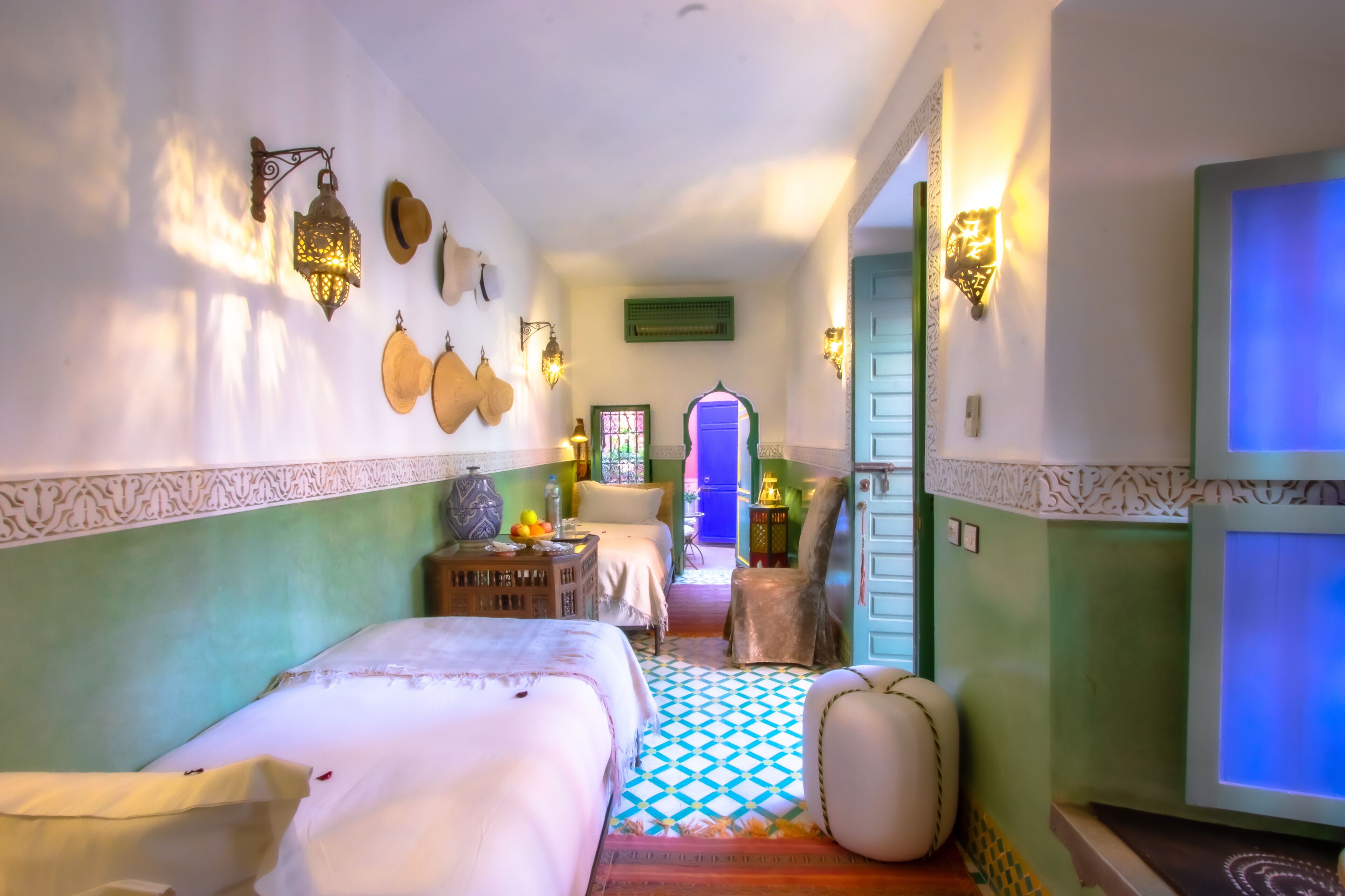A room with a bed, a chair, a table with fruit, and decorative wall hangings.
