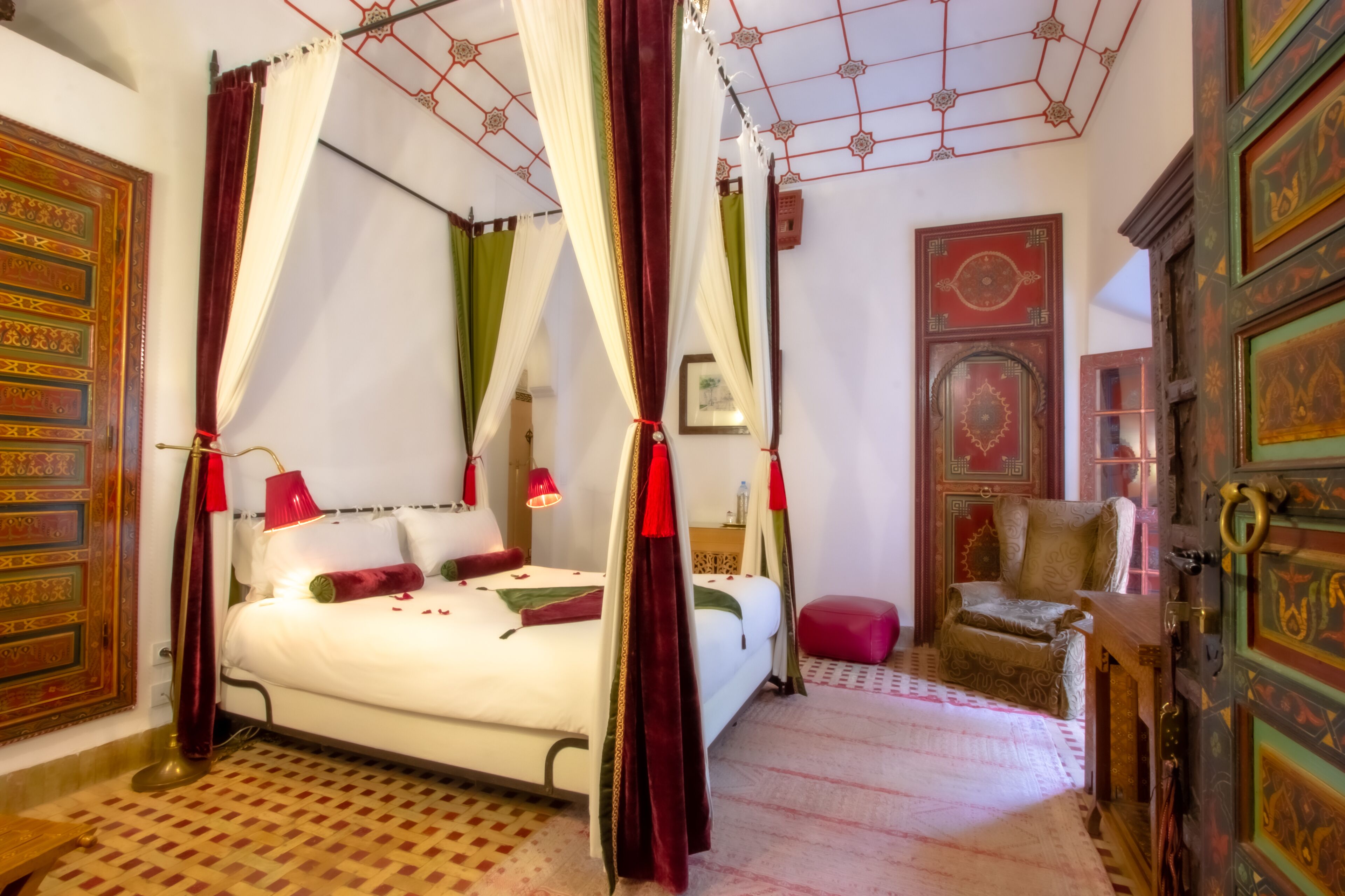 A four-poster bed with red and white drapes, a wooden floor, and a red chair.