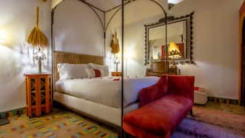 Un dormitorio con cama con dosel, una silla roja, un tapiz estampado y un espejo con marco decorativo.