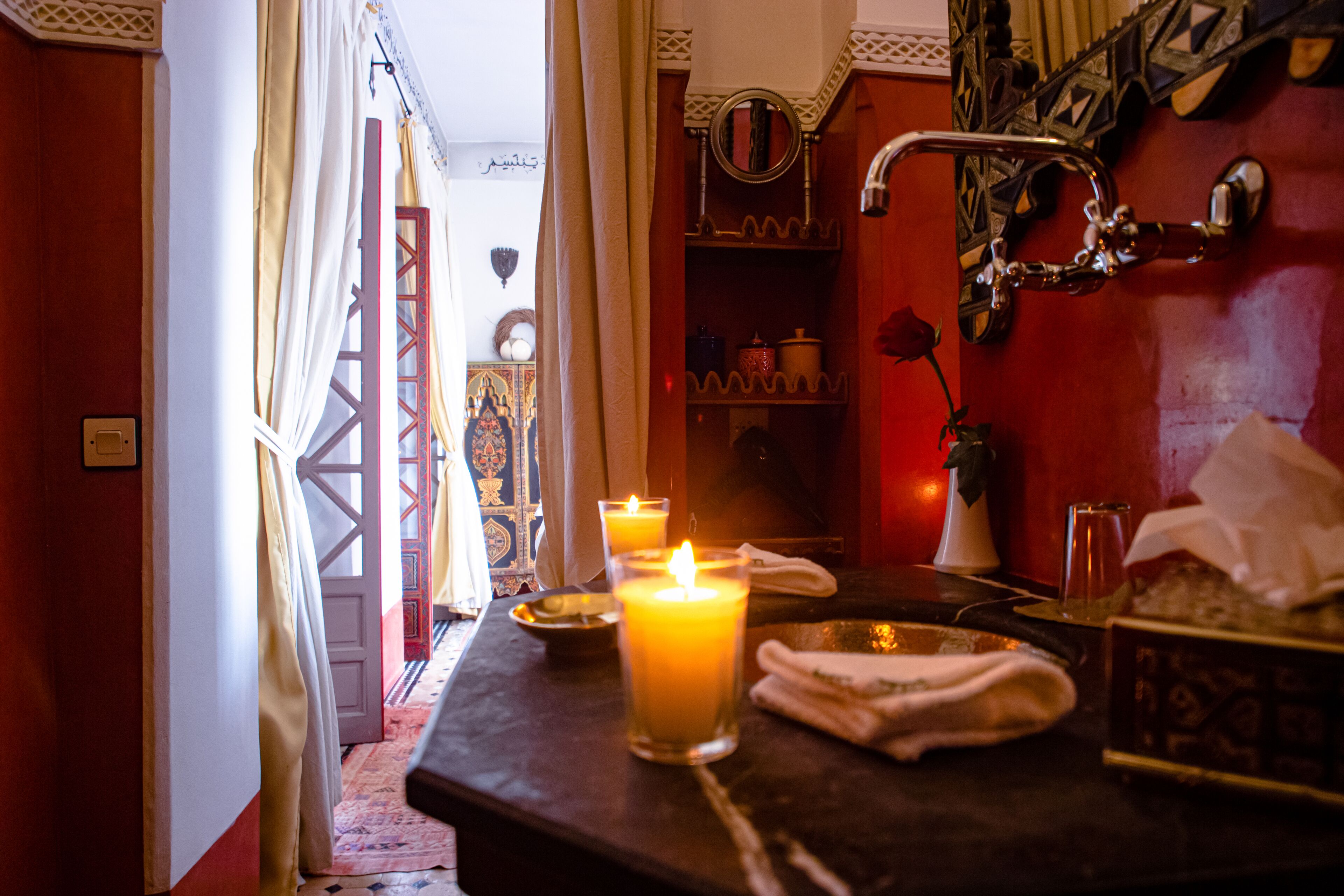 A room with a candle-lit table, a mirror, and a red wall.