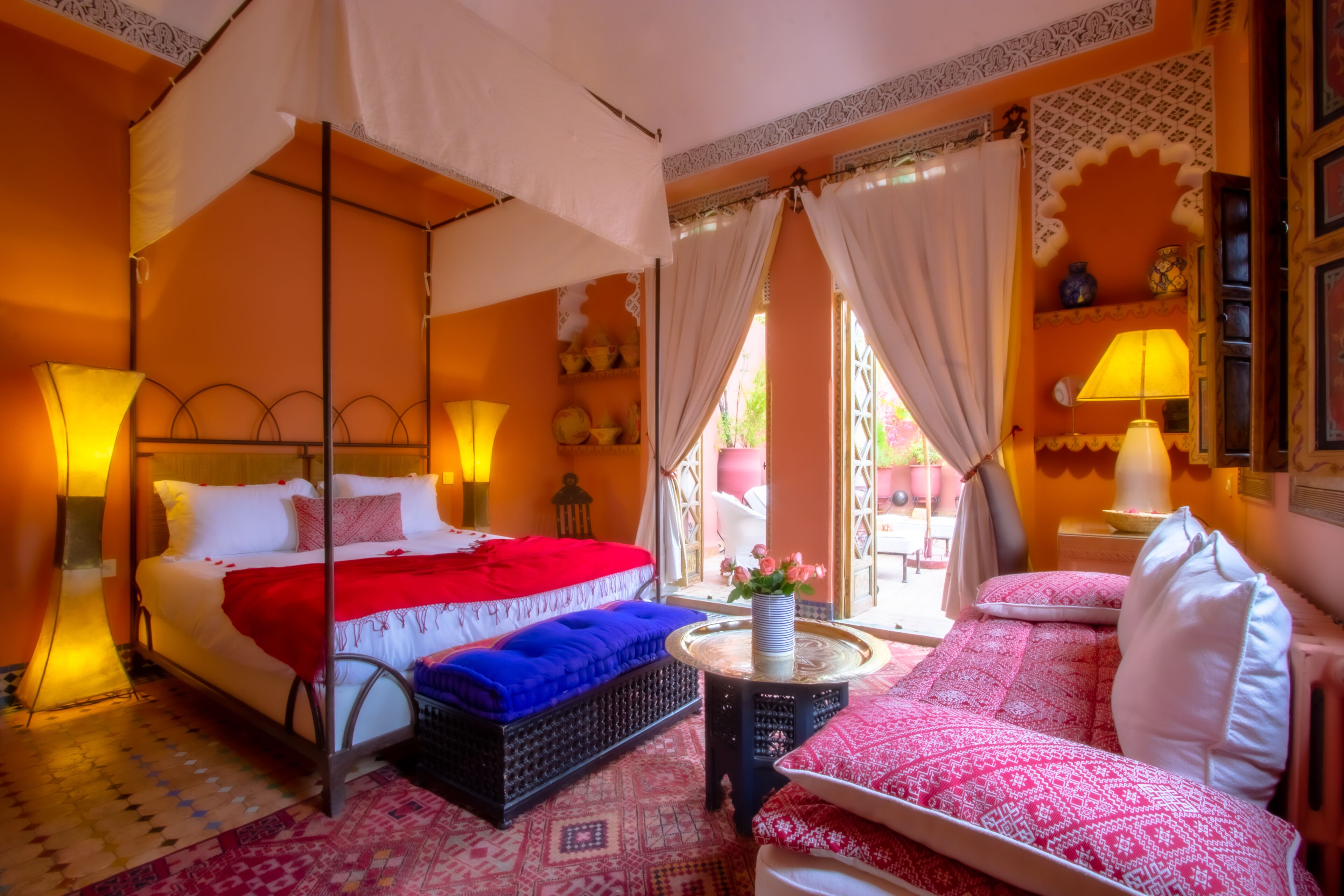 Une chambre dotée d’un lit à baldaquin, d’un canapé, d’une petite table avec un vase, et offrant une vue sur l’extérieur.