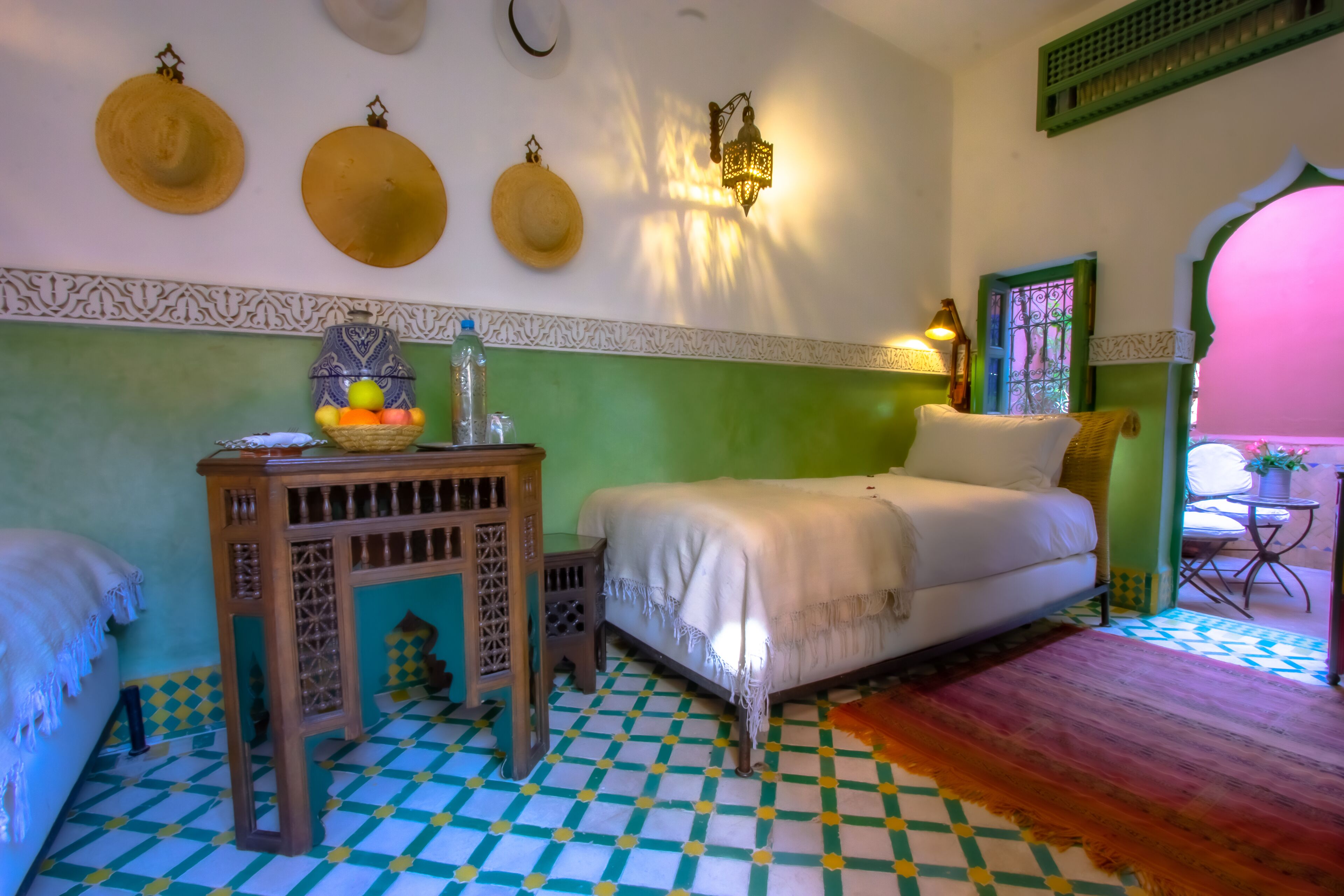 A room with a bed, a small table with a basket of fruit, and a patterned floor.