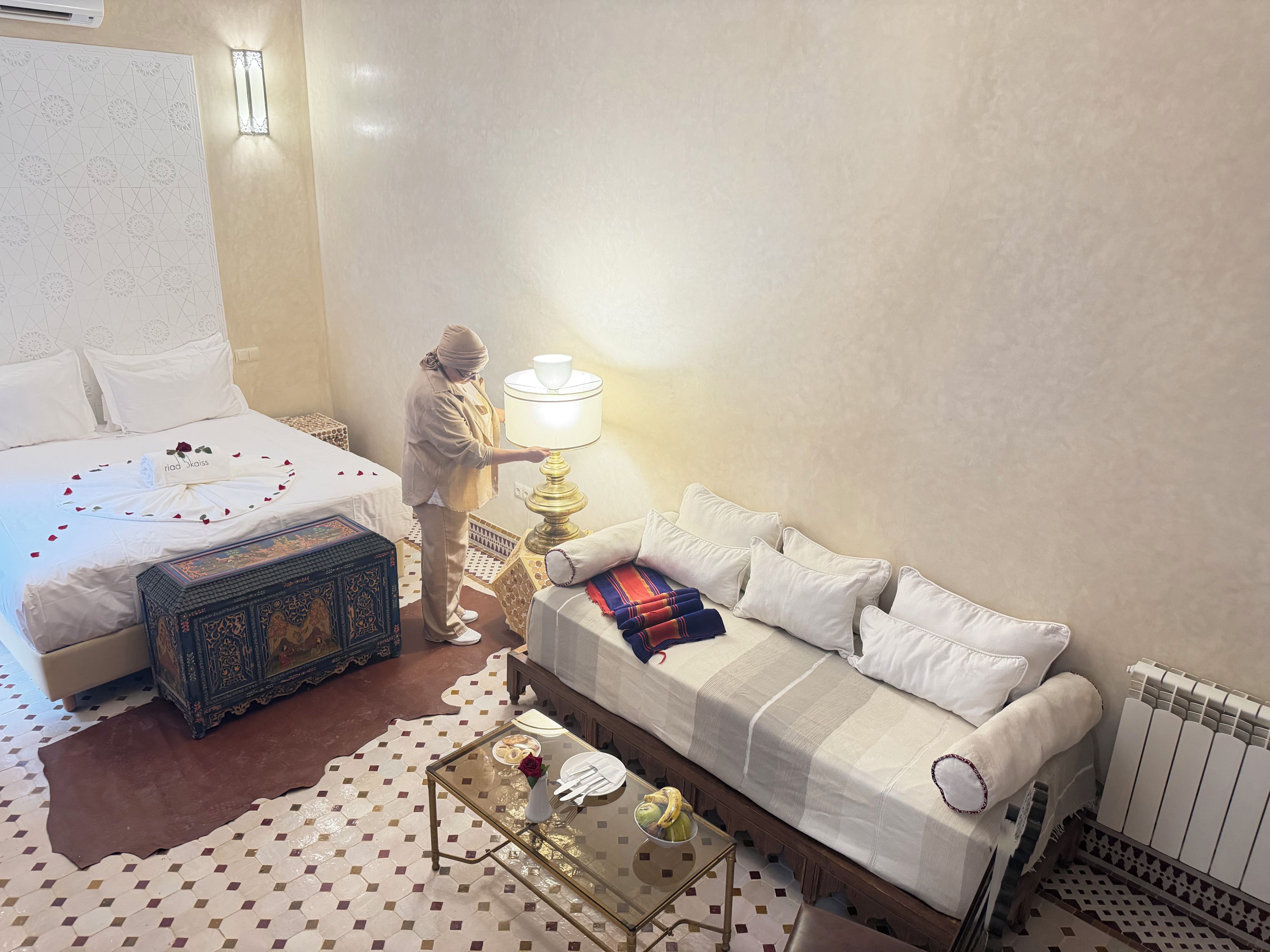 A hotel room with a bed, a sofa, a table with a vase and a banana, and a decorative box.