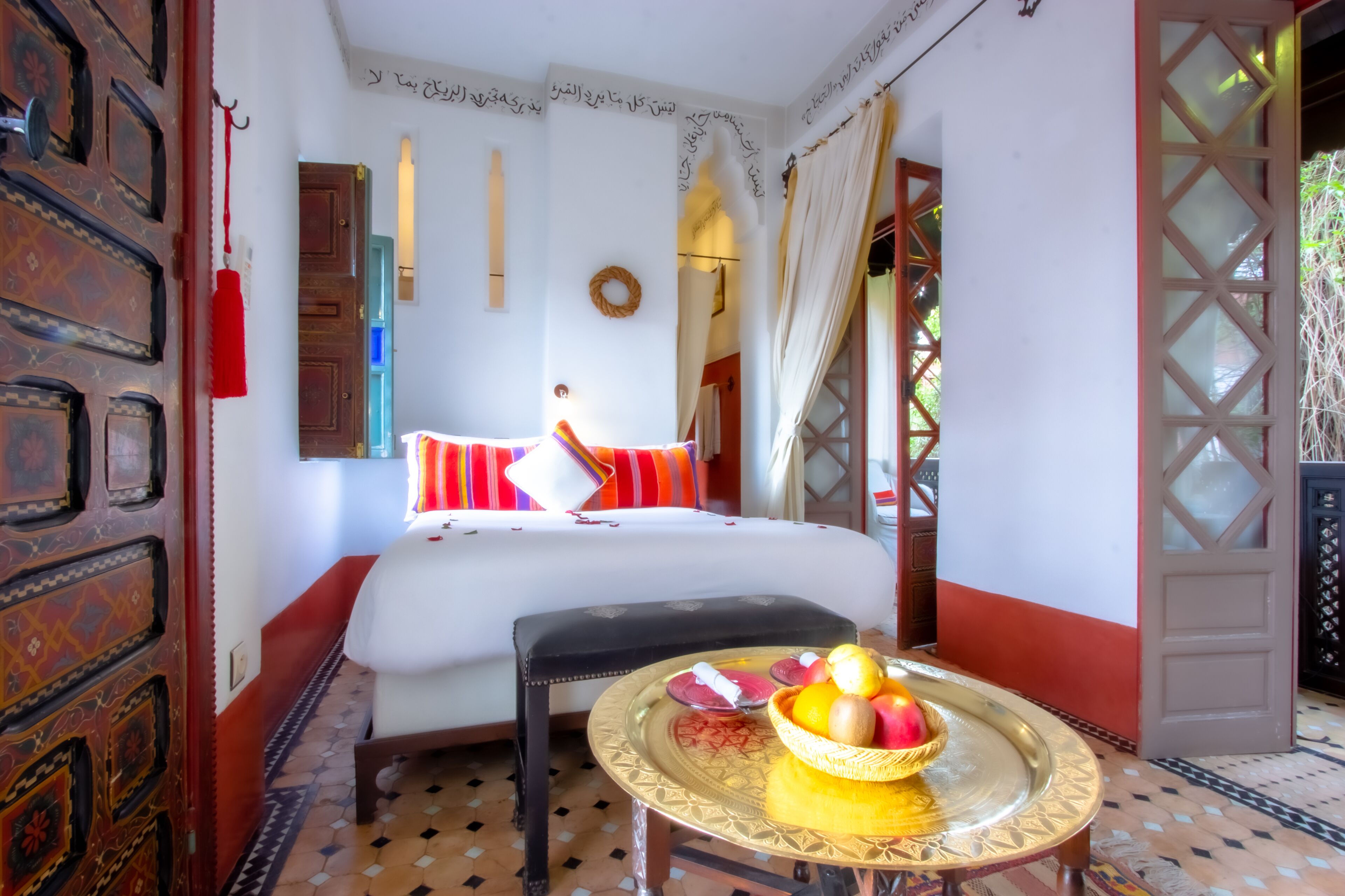 A room with a bed, a small table with fruit, a decorative wall, and a patterned floor.
