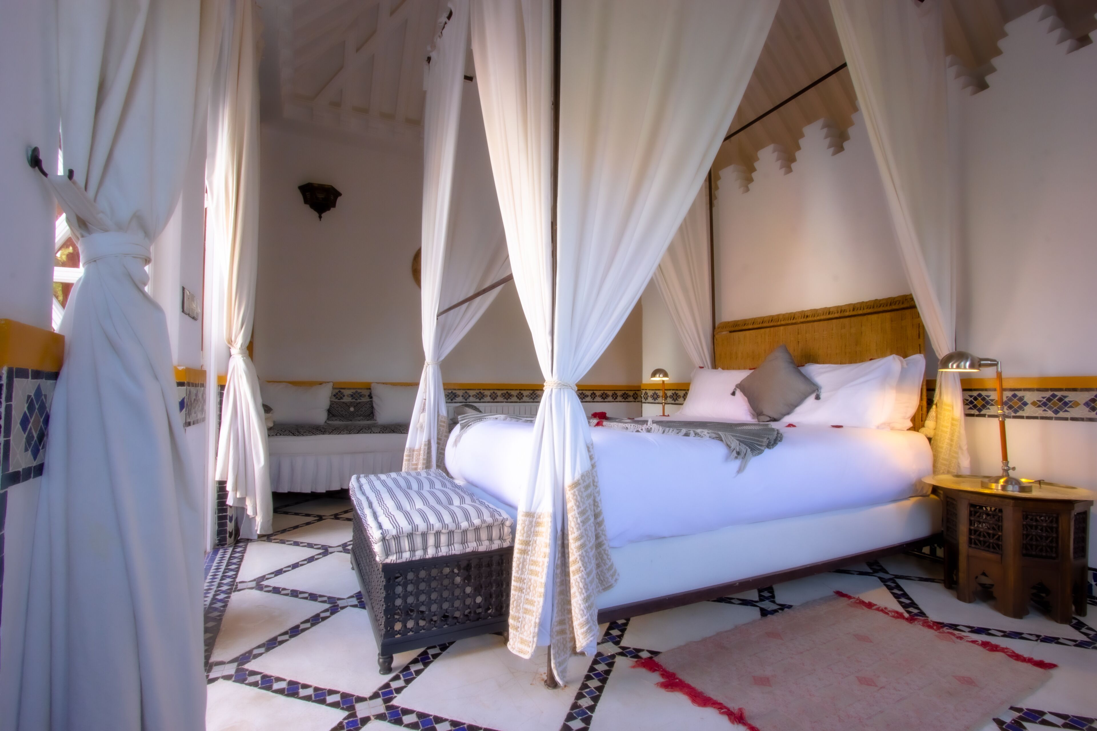 Una habitación con cama, mesita de noche, lámpara y un banco.