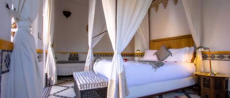 Una habitación con cama, mesita de noche, lámpara y un banco.