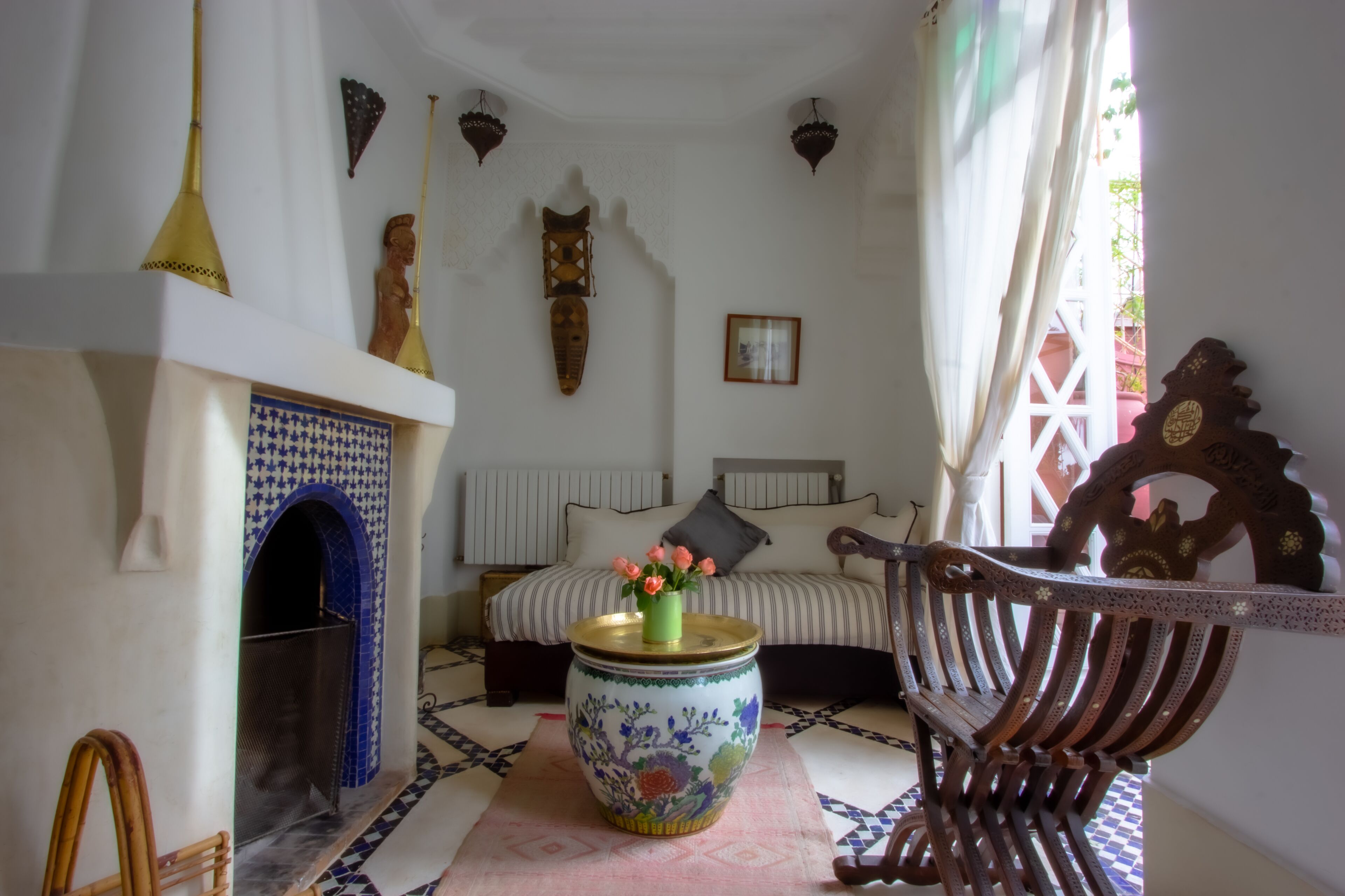 Une pièce comprenant un lit, un vase décoratif avec des fleurs, un banc en bois et un sol à motifs.