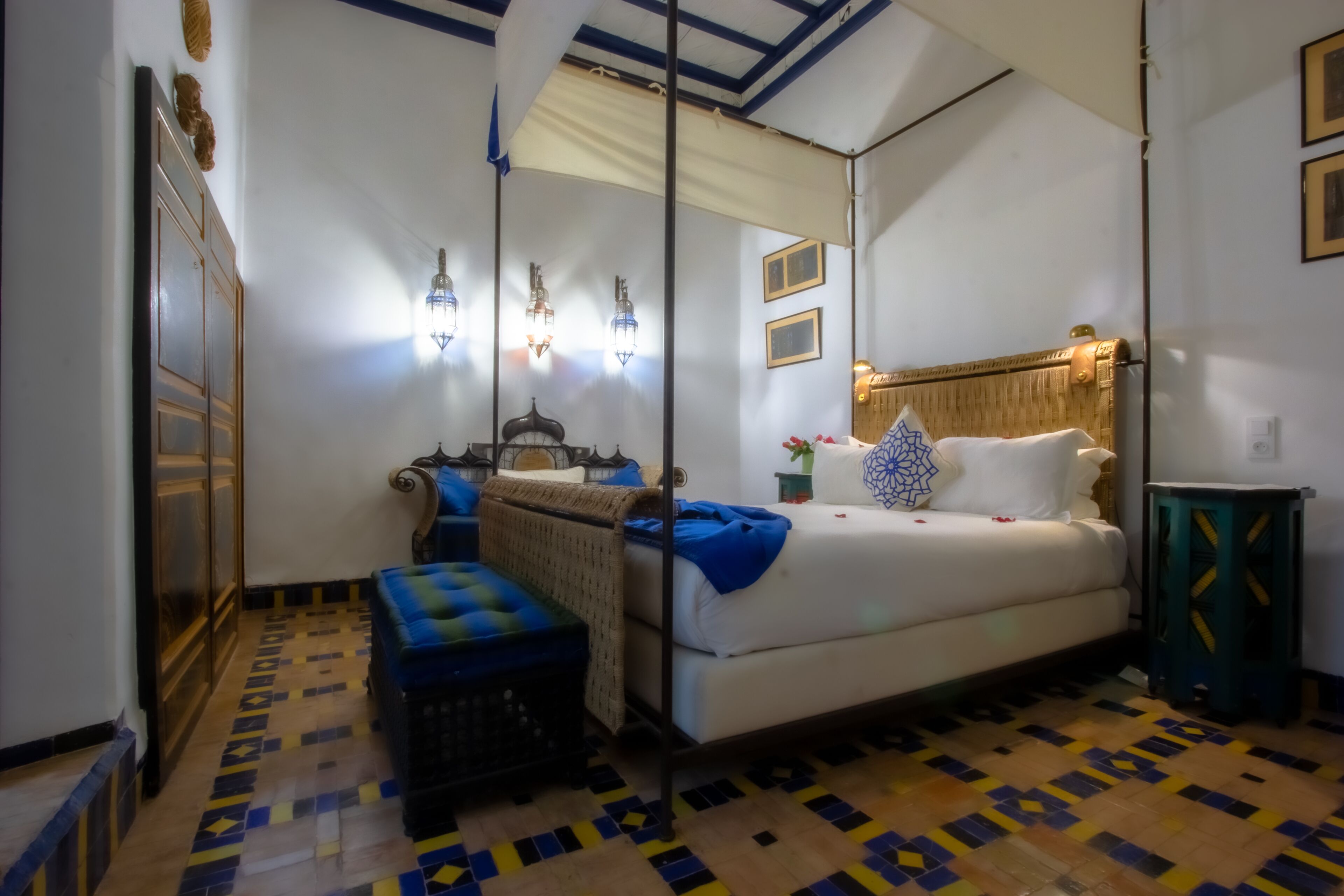 A bedroom with a bed, a nightstand, a lamp, a mirror, and a patterned floor.