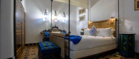 A bedroom with a bed, a nightstand, a lamp, a mirror, and a patterned floor.
