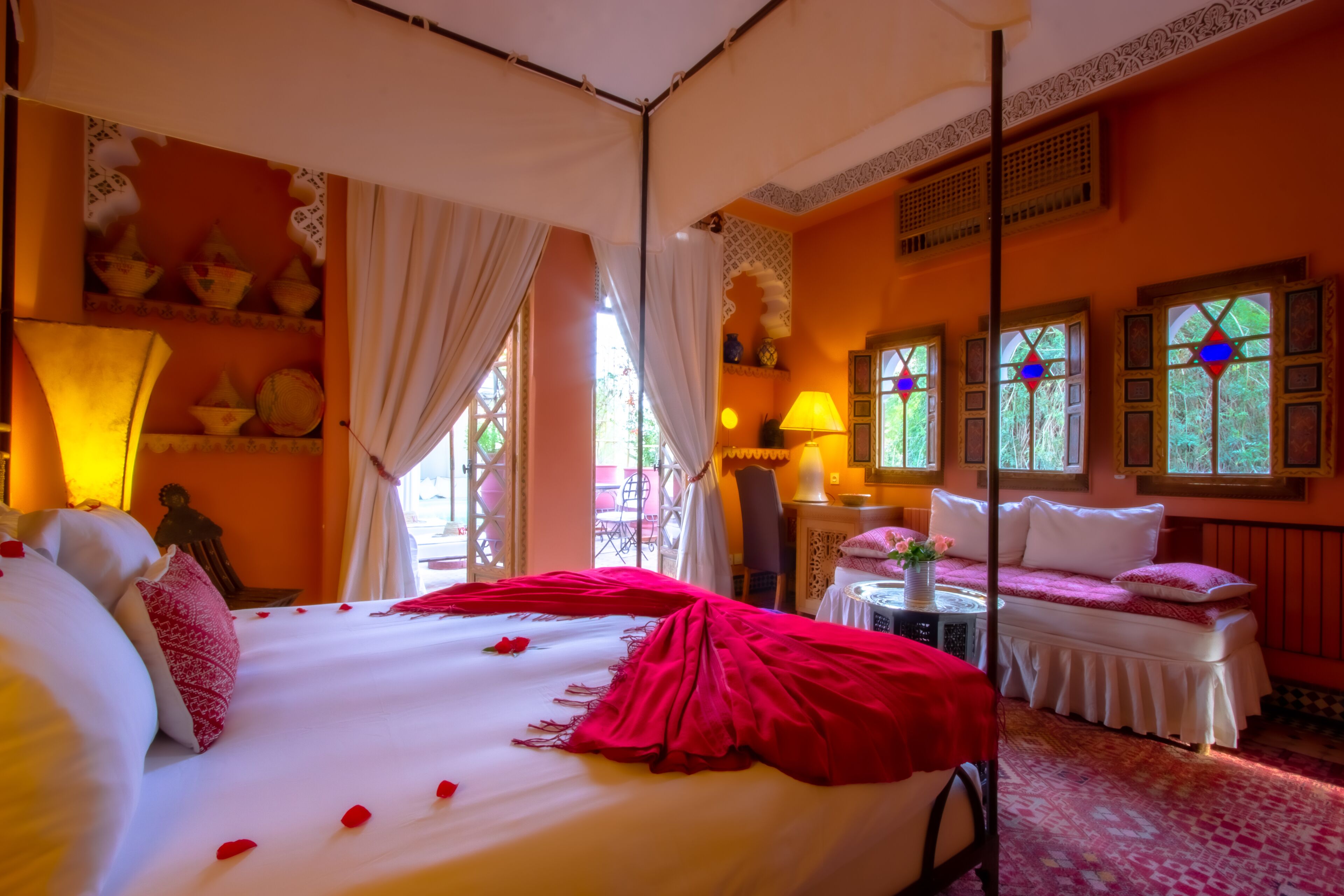 A room with a large bed, a bench, and a small table with a lamp.