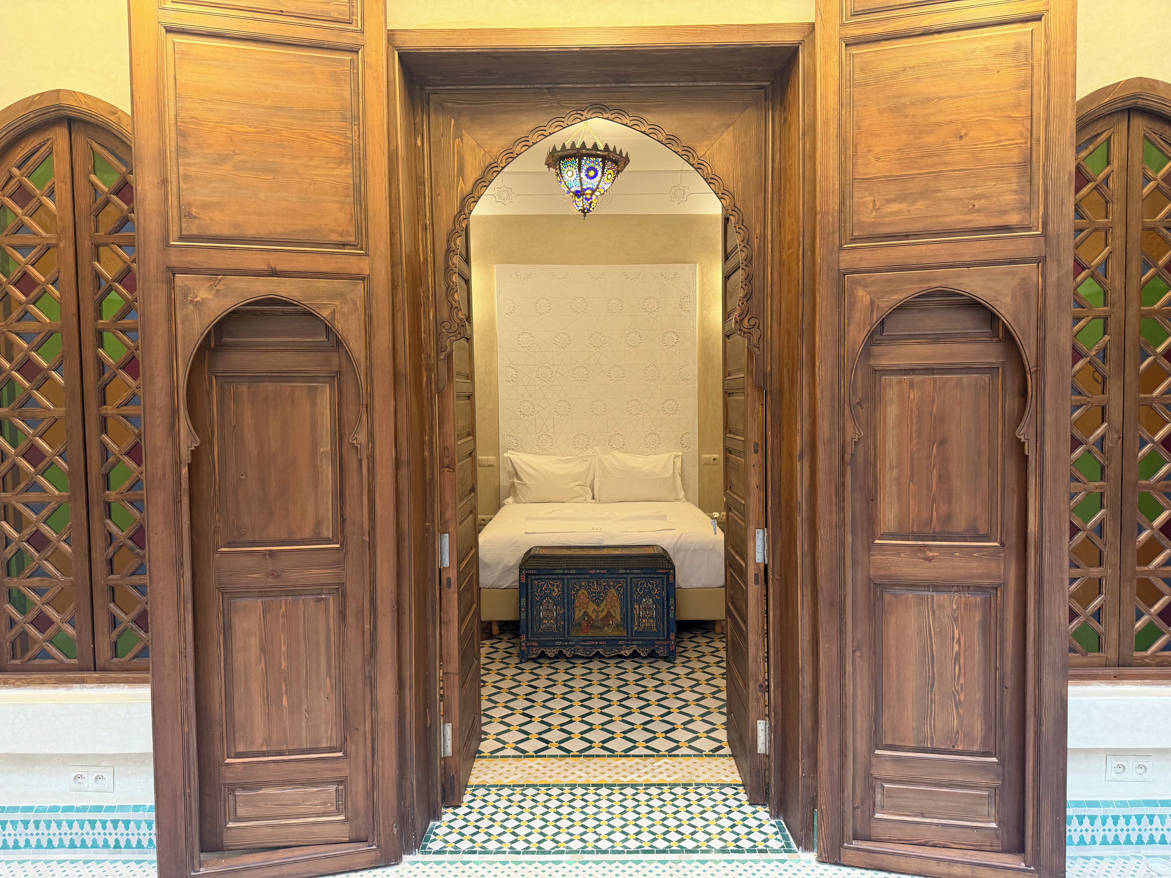 Un estrecho vano con puertas de madera y una cama con ropa blanca.