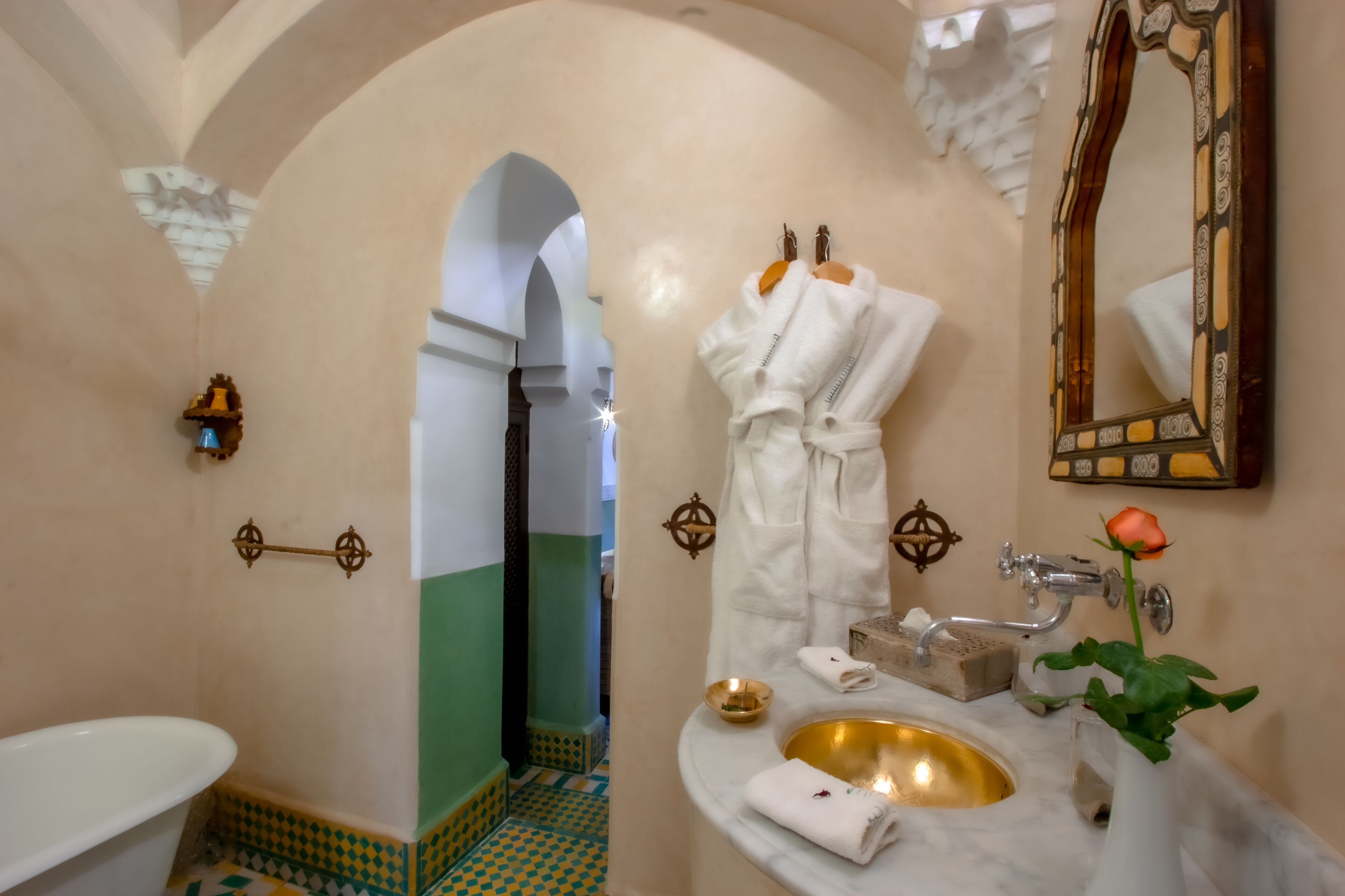A bathroom with a white bathtub, a gold sink, and a mirror with a decorative frame.
