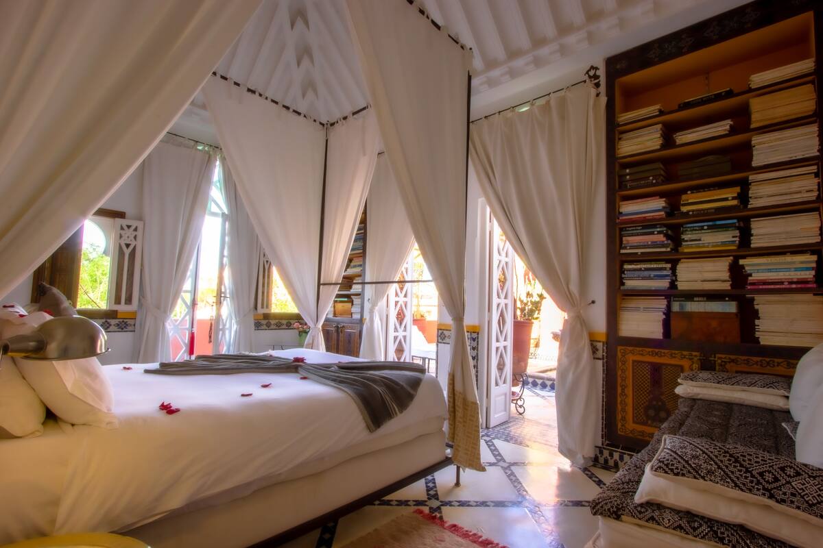 A room with a bed, a bookshelf, and a view of the outside.
