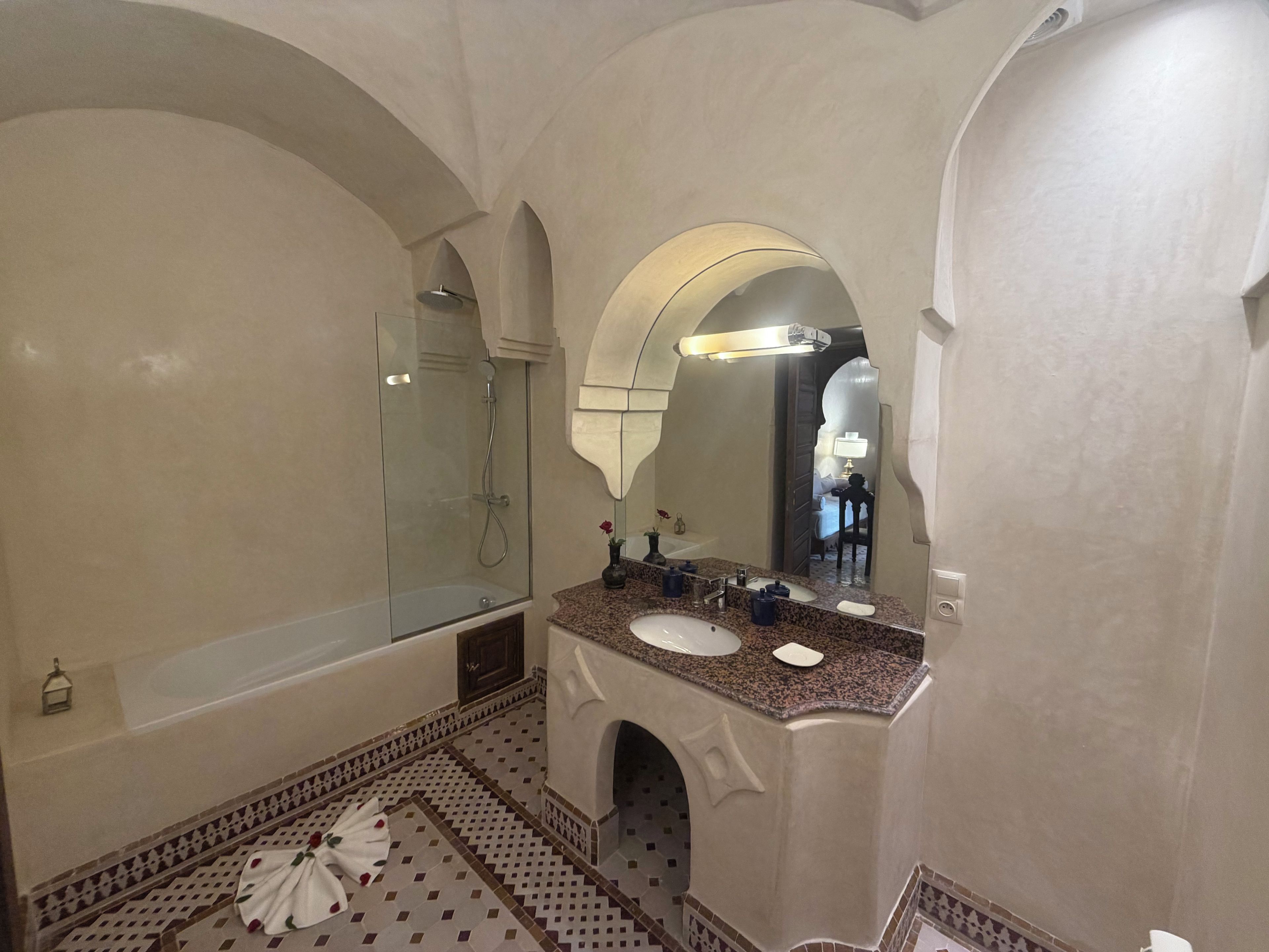 A bathroom with a glass-enclosed shower, a sink with a marble countertop, and a large mirror.