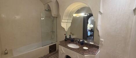 A bathroom with a glass-enclosed shower, a sink with a marble countertop, and a large mirror.