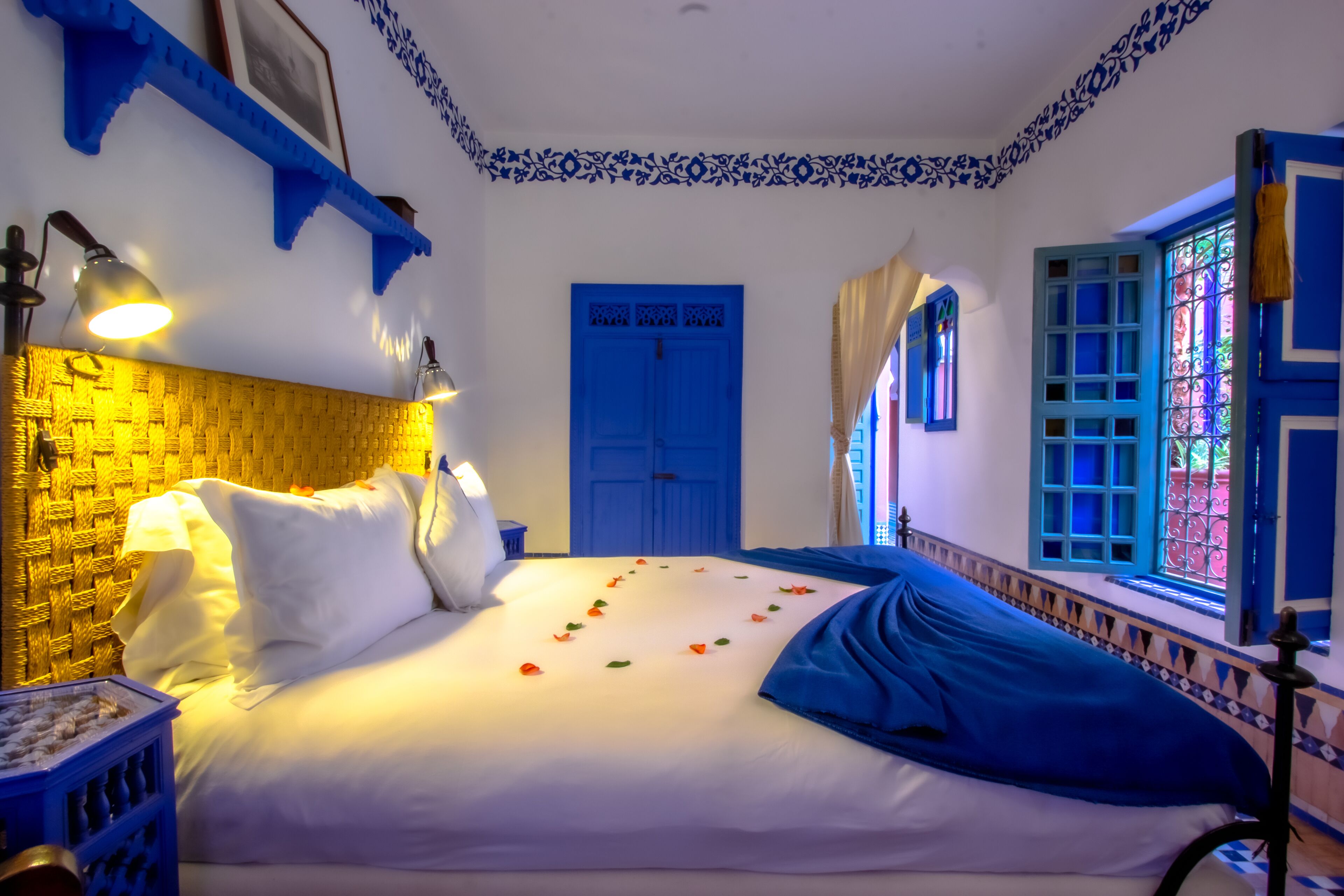 A room with a bed, a blue door, and a window with blue shutters.