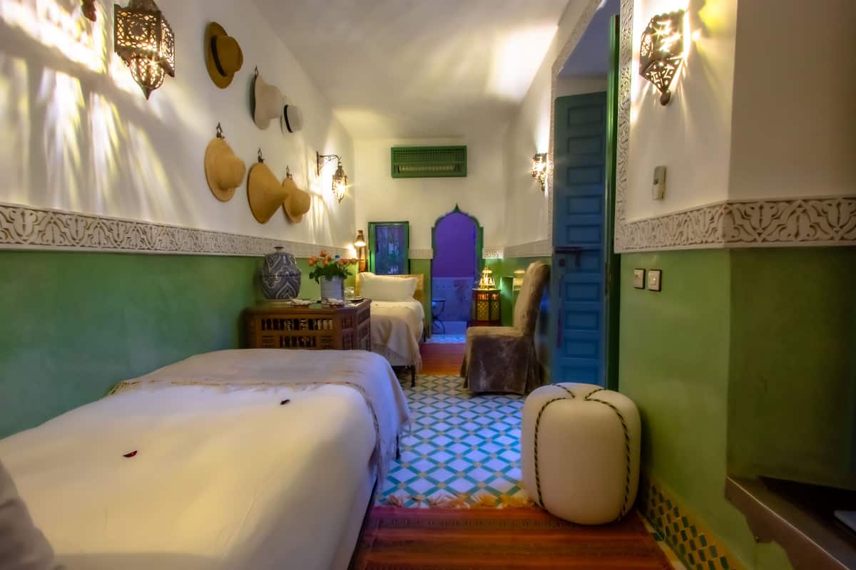 A narrow hallway with two beds, a patterned floor, and decorative wall sconces.