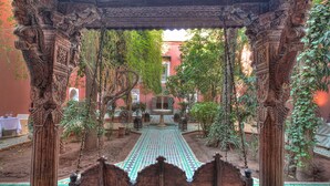 An ornate courtyard with intricate wooden carvings, a tiled pathway, and lush greenery. - Riad Kaiss by Anika (Marrakech)