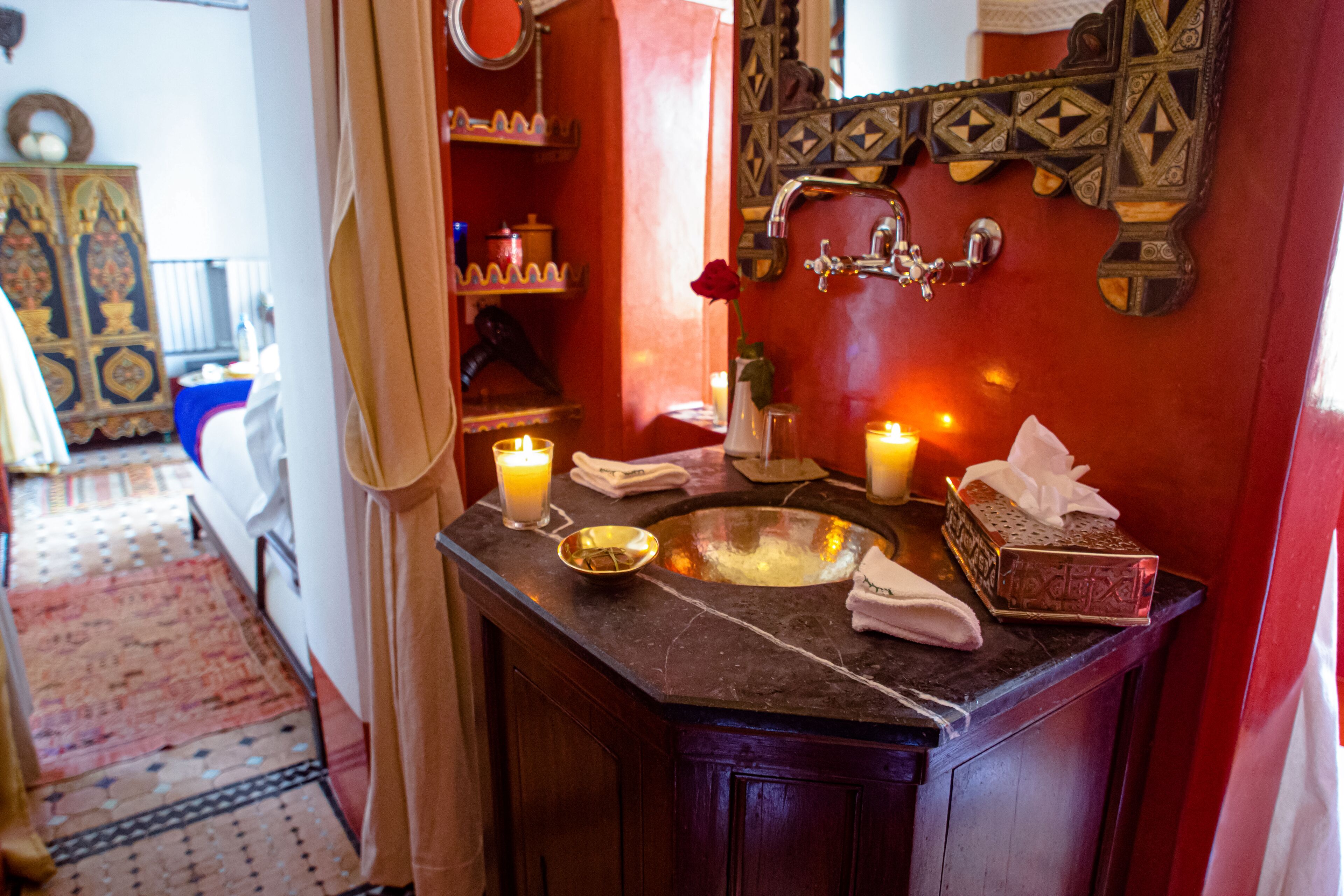 Un baño con lavamanos de mármol oscuro, velas, un espejo decorativo y una pequeña pila de bronce.
