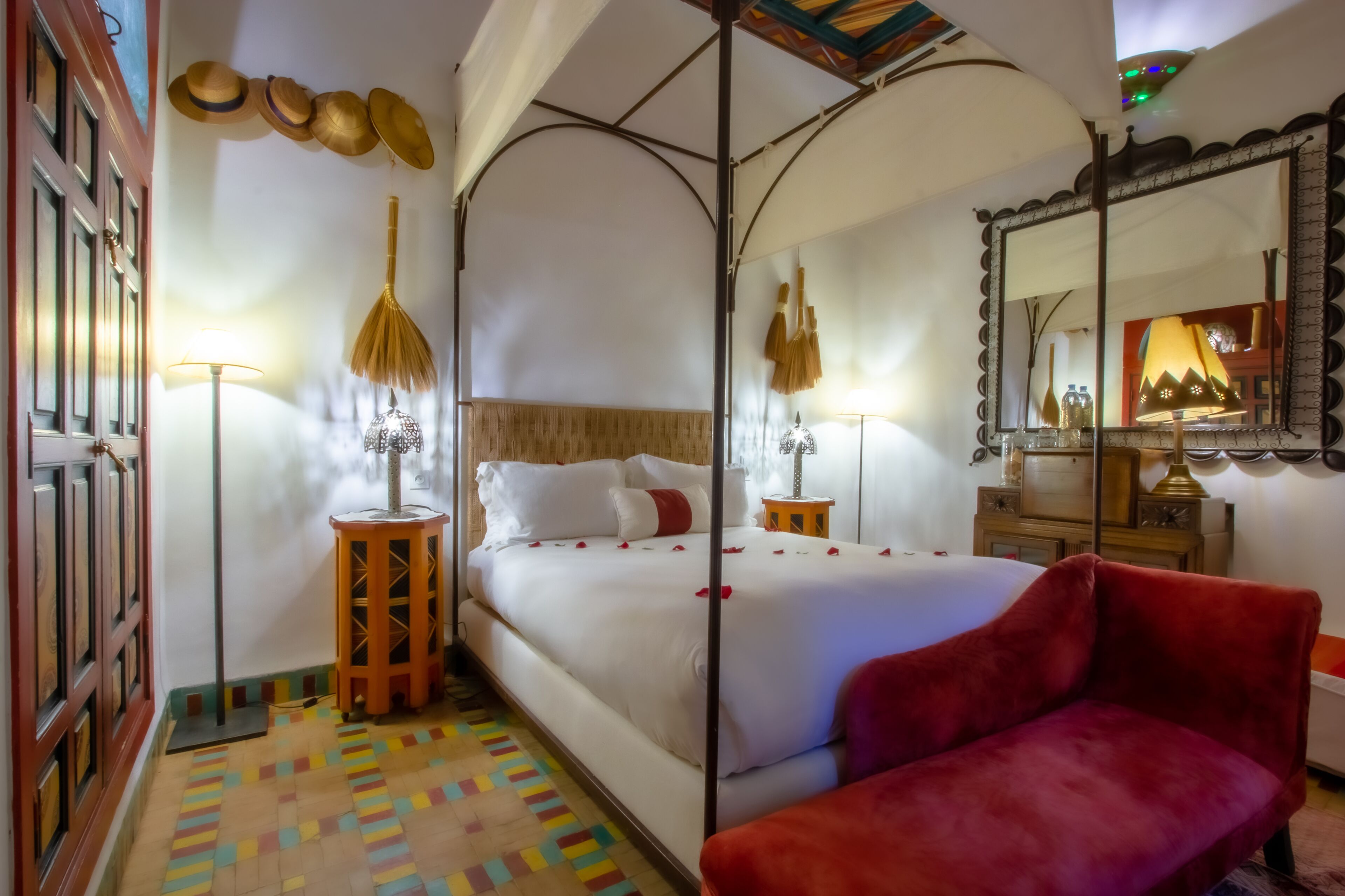 Ein Zimmer mit einem großen Bett, einem roten Sessel, einem Spiegel und einem gemusterten Boden.