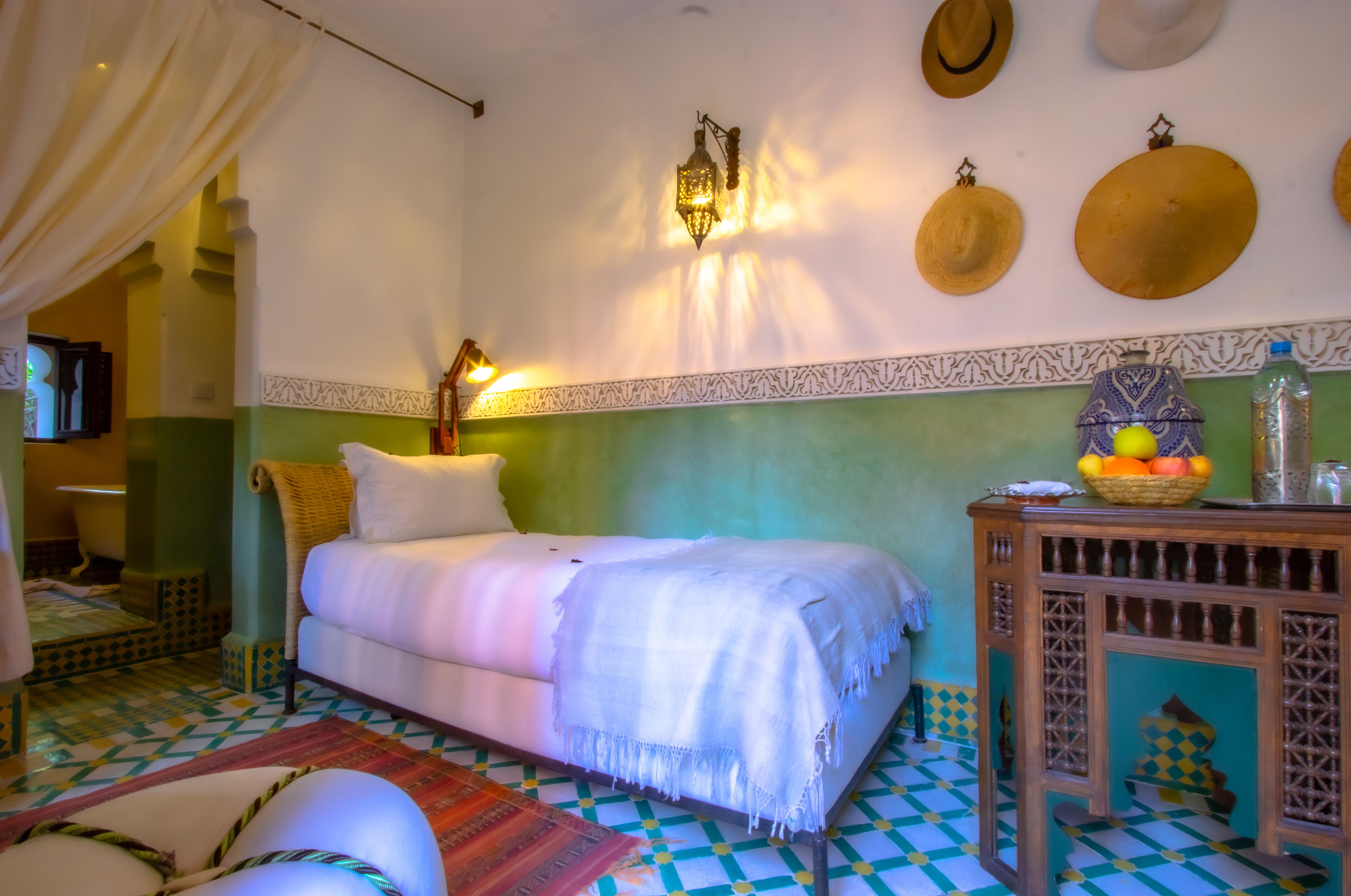 A room with a bed, a nightstand, a wall-mounted lamp, and a decorative wall with hats.