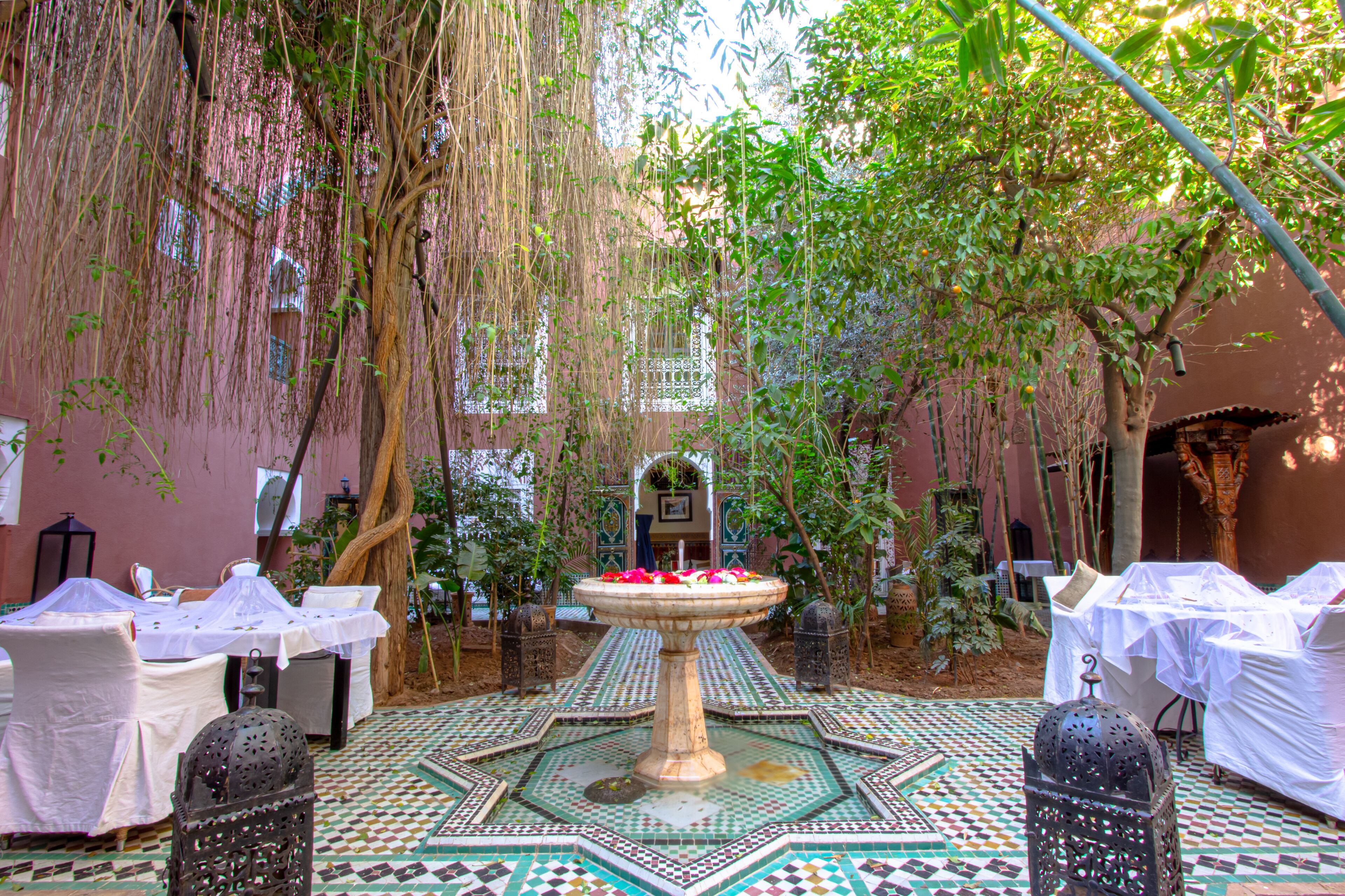 An outdoor courtyard with a fountain, tables, chairs, and a tiled floor.