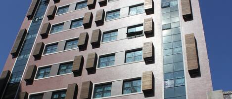 Un edificio de gran altura con varios pisos, que presenta una combinación de ventanas rectangulares y cuadradas, algunas con unidades de aire acondicionado externas.