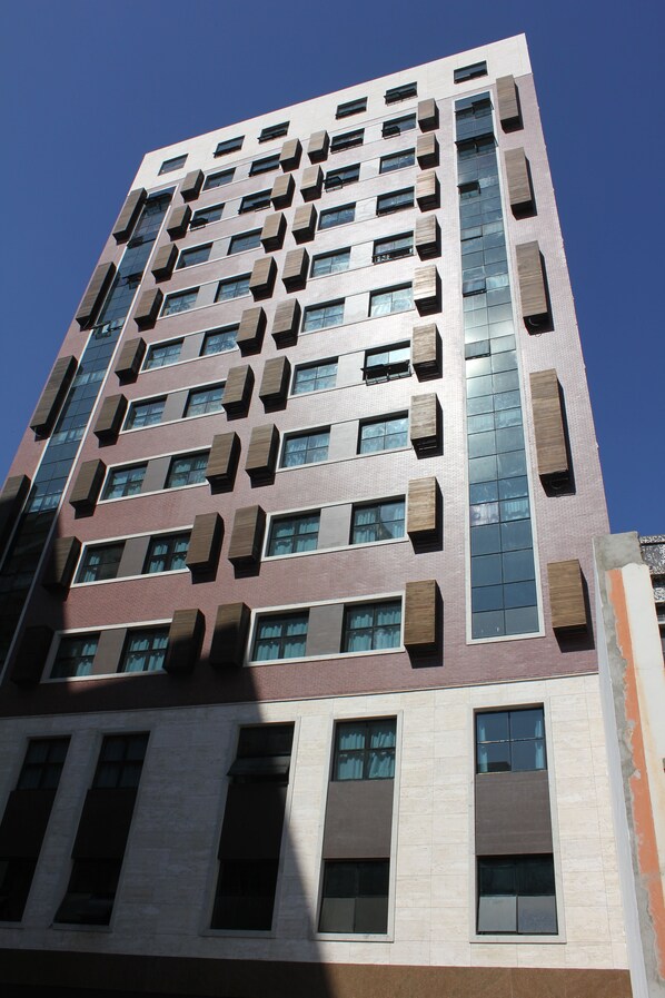 Un edificio de gran altura con varios pisos, que presenta una combinación de ventanas rectangulares y cuadradas, algunas con unidades de aire acondicionado externas.