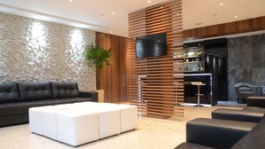 Un salon moderne avec un canapé en cuir noir, un pouf blanc et un téléviseur fixé sur un mur en lambris de bois.