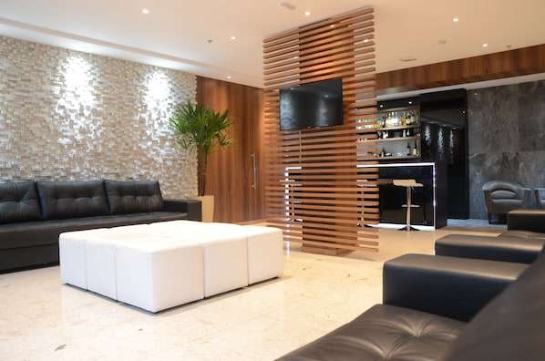 Ein modernes Wohnzimmer mit einem schwarzen Ledersofa, einem weißen Hocker und einem Fernseher, der an einer Holzlattenwand befestigt ist.
