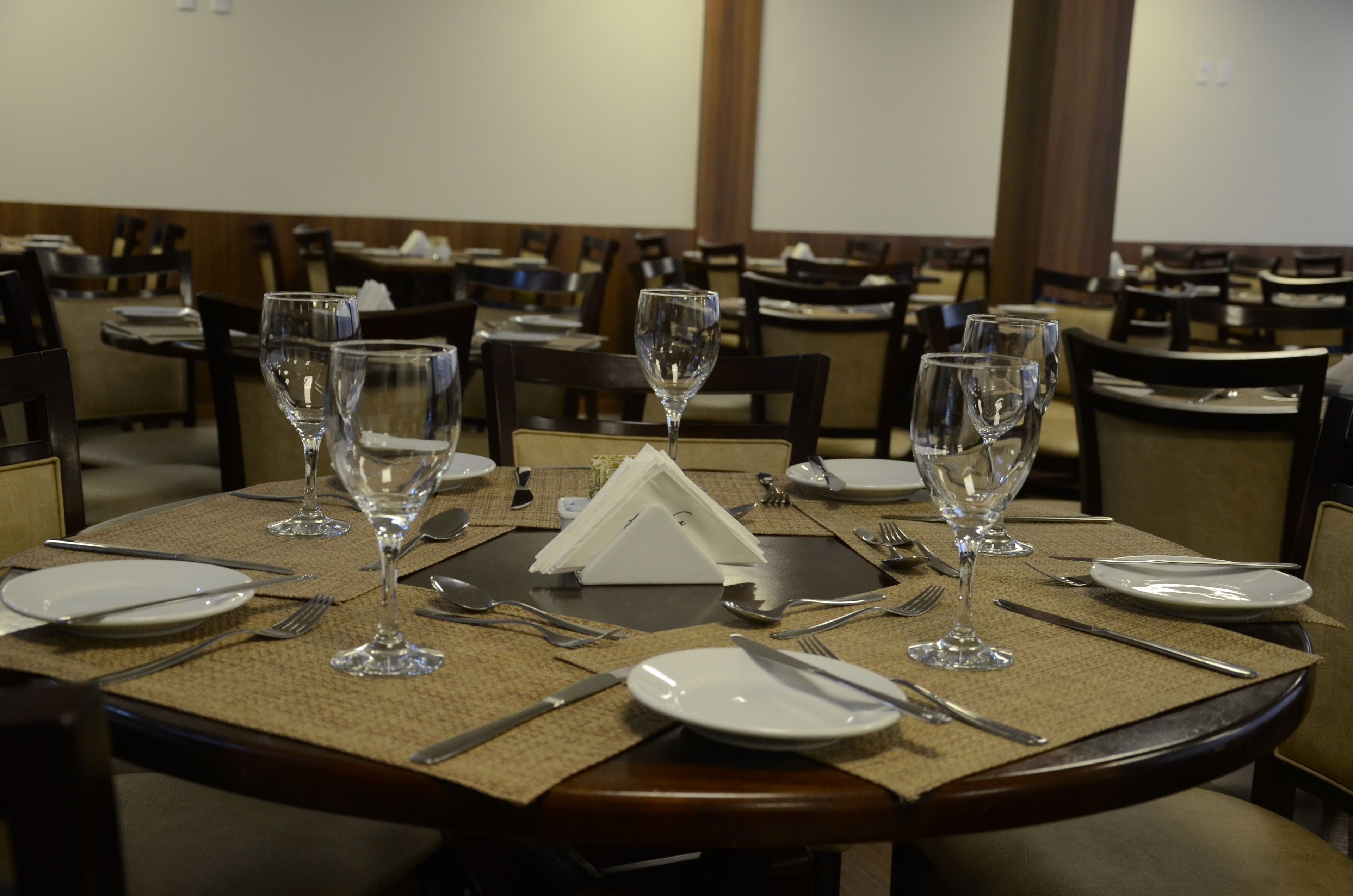 Un tavolo da pranzo apparecchiato con bicchieri da vino, piatti, posate e un portatovaglioli, in un ristorante con diversi tavoli e sedie.