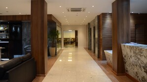Un hall d’hôtel moderne avec un long plancher poli, des panneaux de bois, un comptoir de réception et un espace salon comprenant un canapé et un bar.