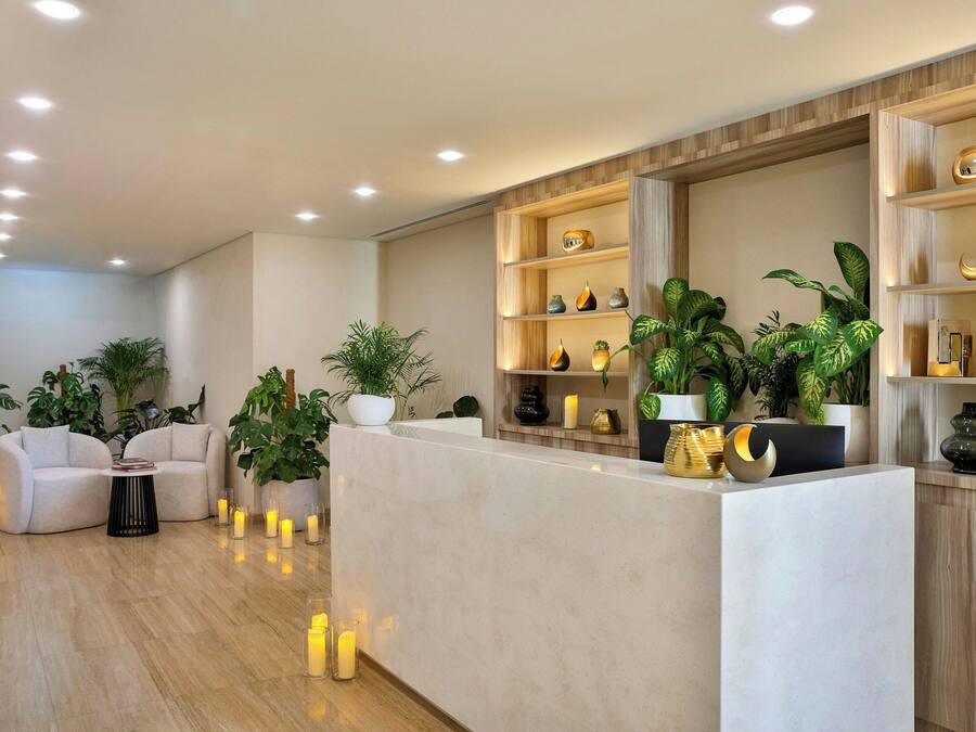 A modern reception area with a marble reception desk, potted plants, and a seating area with a sofa and a small table.