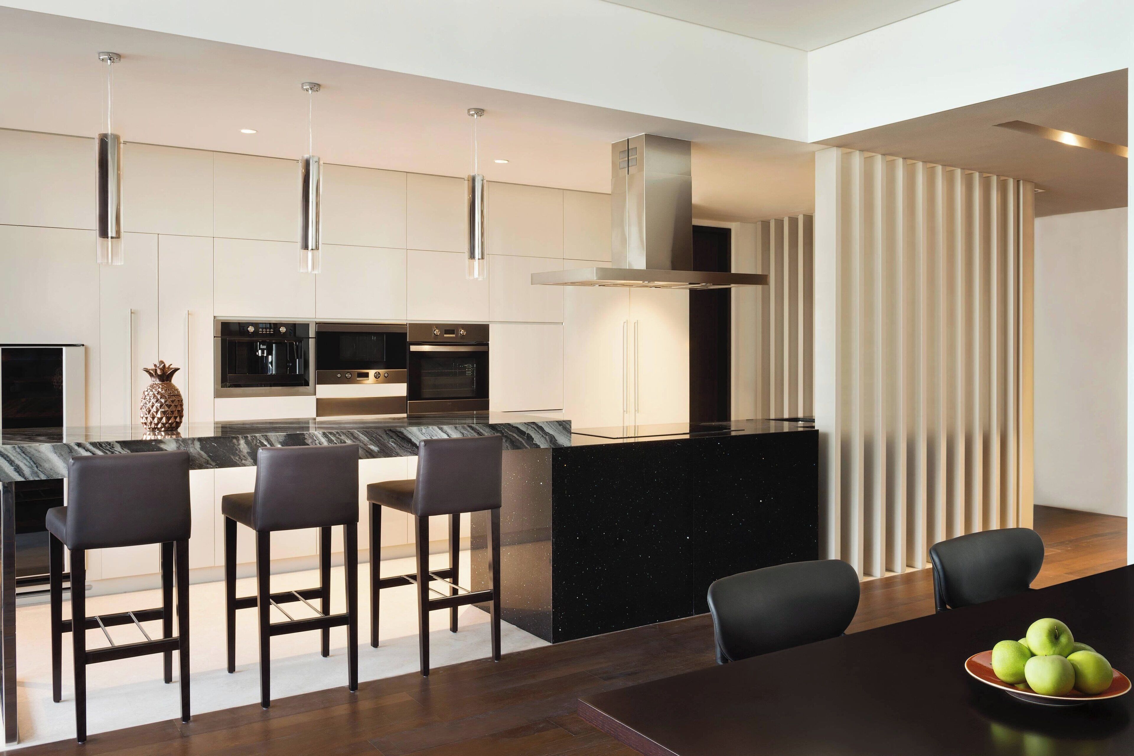 A modern kitchen with a black countertop, stainless steel appliances, and a central island with bar stools.