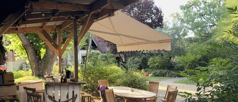 An outdoor patio with a wooden pergola, a round table, and several chairs.