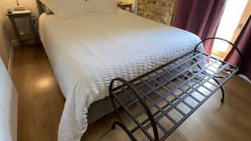 Una cama bien hecha con estructura metálica, dos mesitas de noche con lámparas, una pared con un cartel que dice 'LOVE HOME' y una pared de piedra con cortina morada.