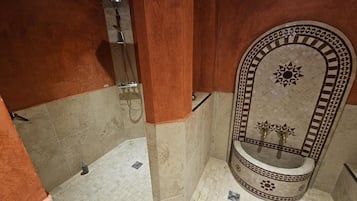 Een badkamer met douche, wastafel en decoratieve betegelde wand.