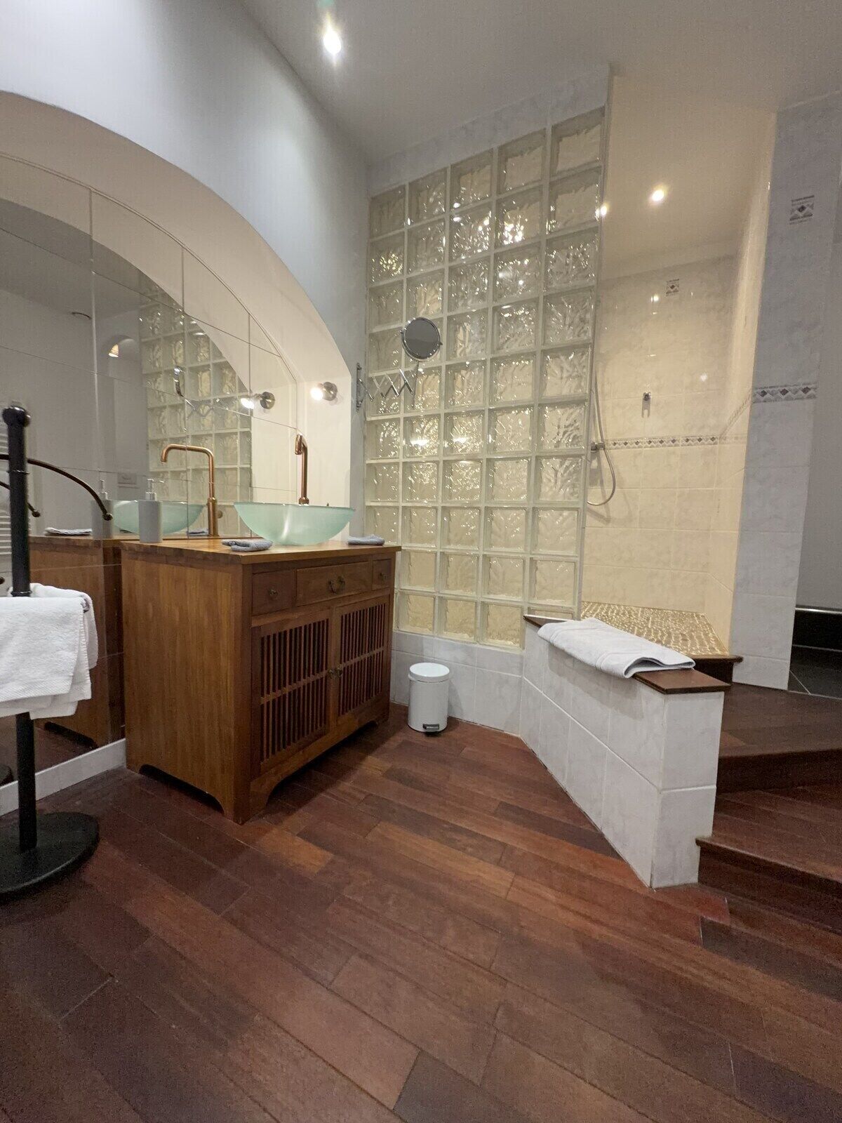 Un baño moderno con tocador de madera, lavabo de vidrio y un espejo grande.