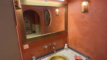 Un baño con un lavamanos dorado, un espejo y un suelo de baldosas estampadas.