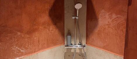 Ducha con cabezal de ducha manual y grifo empotrado en la pared, suelo de azulejos y diseño en esquina.