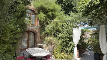 Ein Patio mit rundem Tisch und Stühlen, umgeben von dichtem Grün und einer Backsteinmauer.
