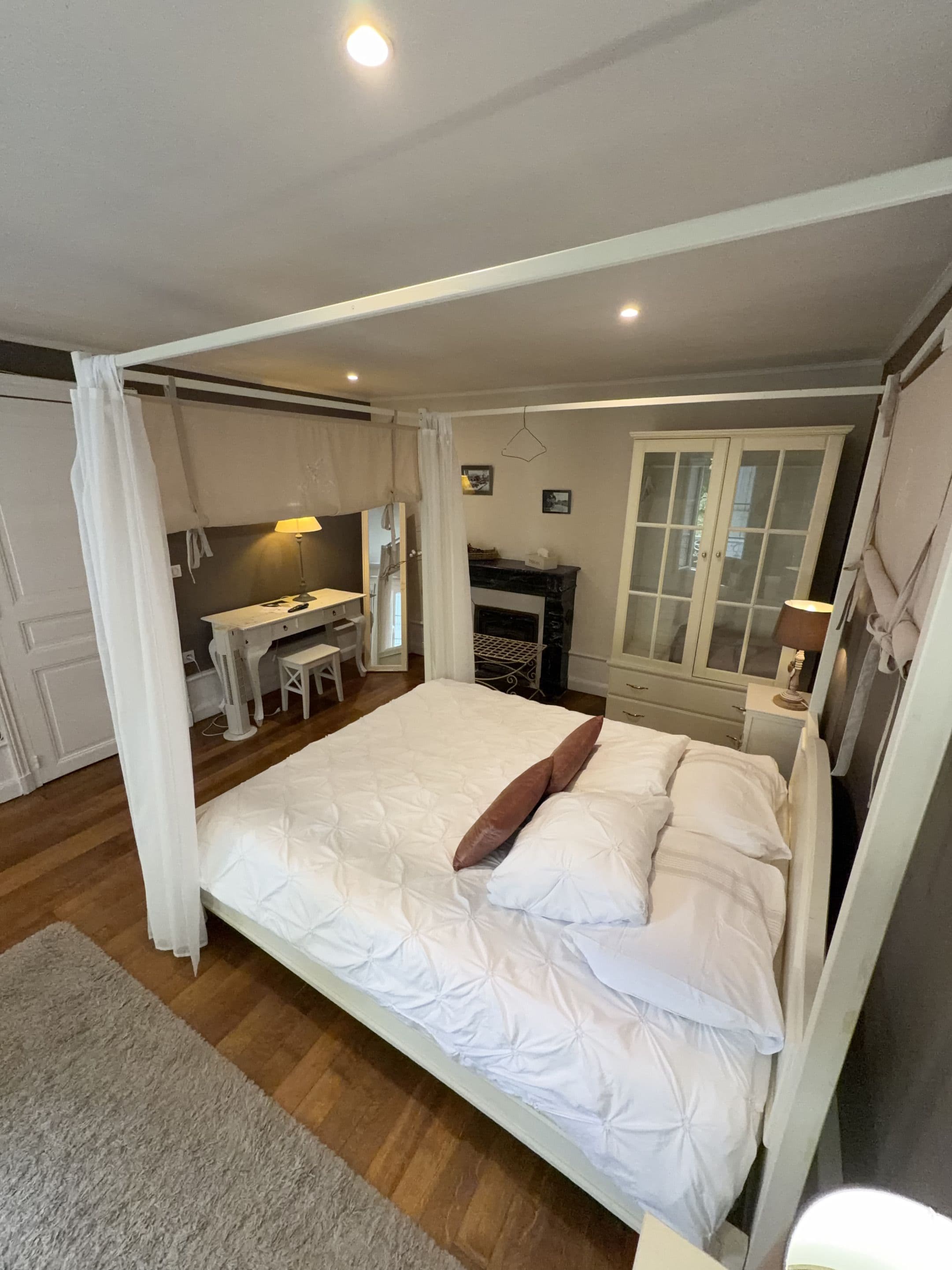 A bedroom with a large bed, a desk, and a fireplace.