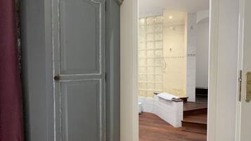 A room with a grey wardrobe, a white door leading to a bathroom with a glass shower enclosure.