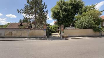 Una entrada con portón, cielo despejado, un árbol alto y un edificio con techo de tejas al fondo.