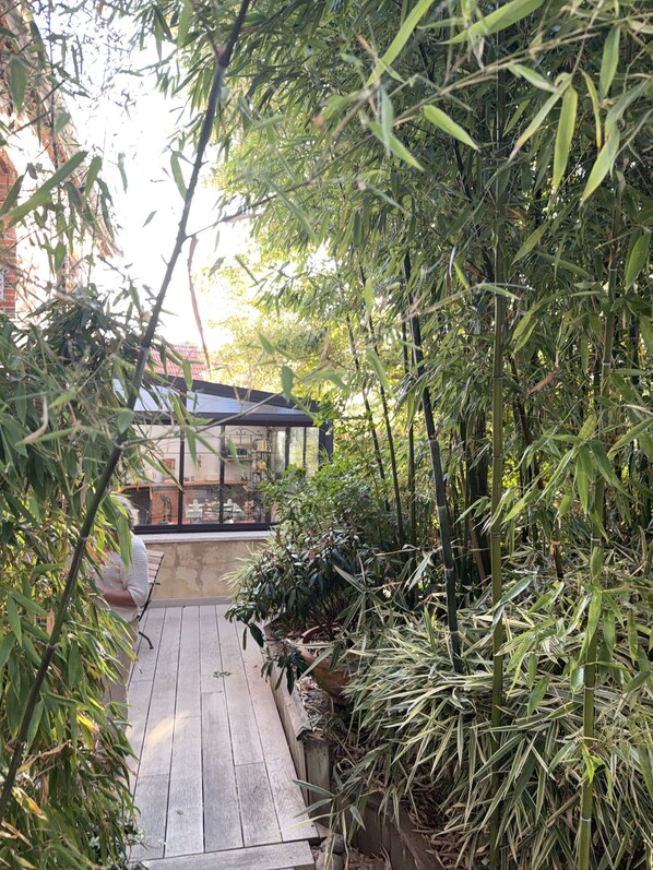 A wooden deck leading to a glass-enclosed area with a view of a building. - Le Corrigot (Pierry)